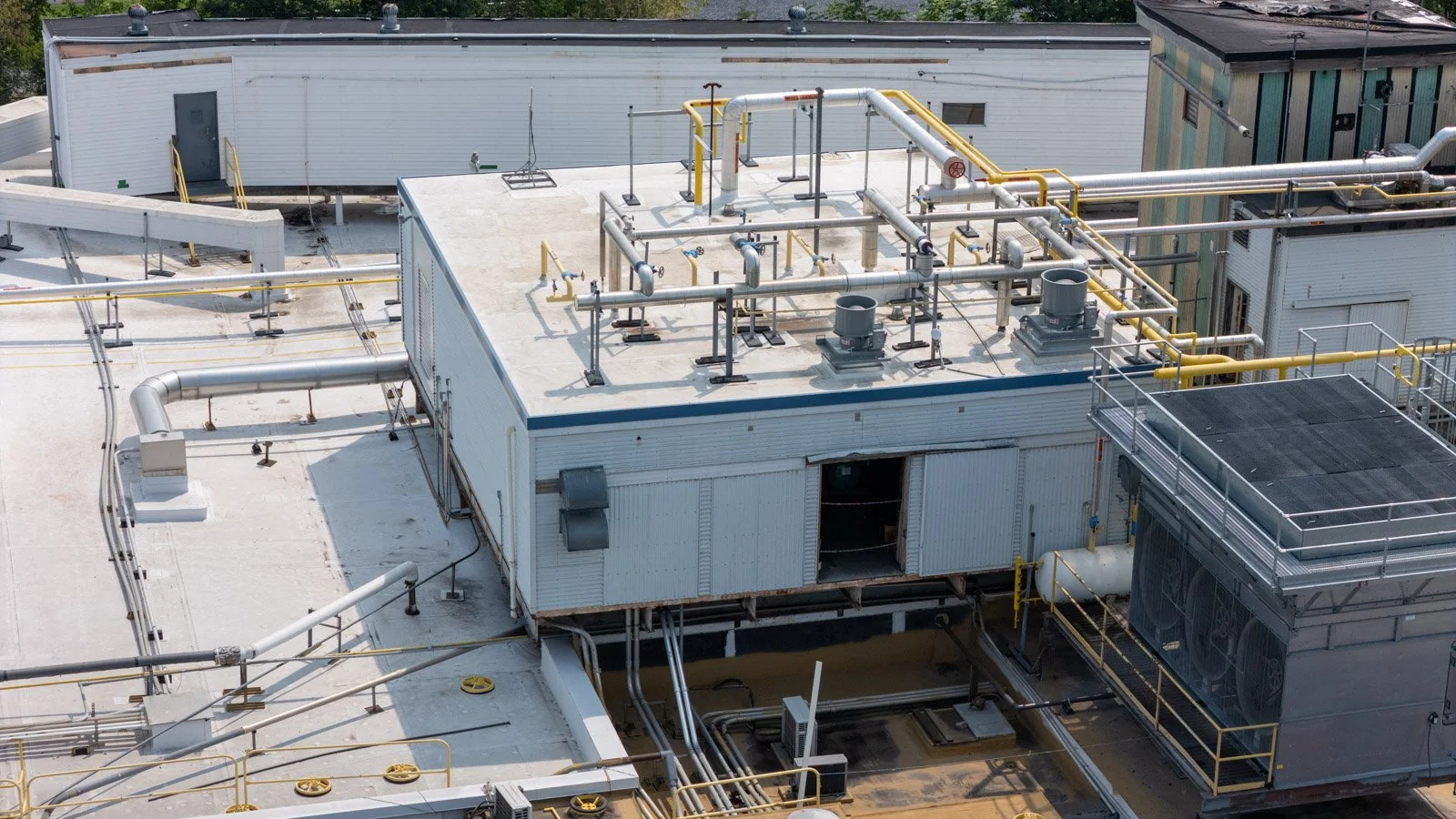 Close aerial view of the commercial roof surrounding industrial piping, ventilation equipment, and access areas.