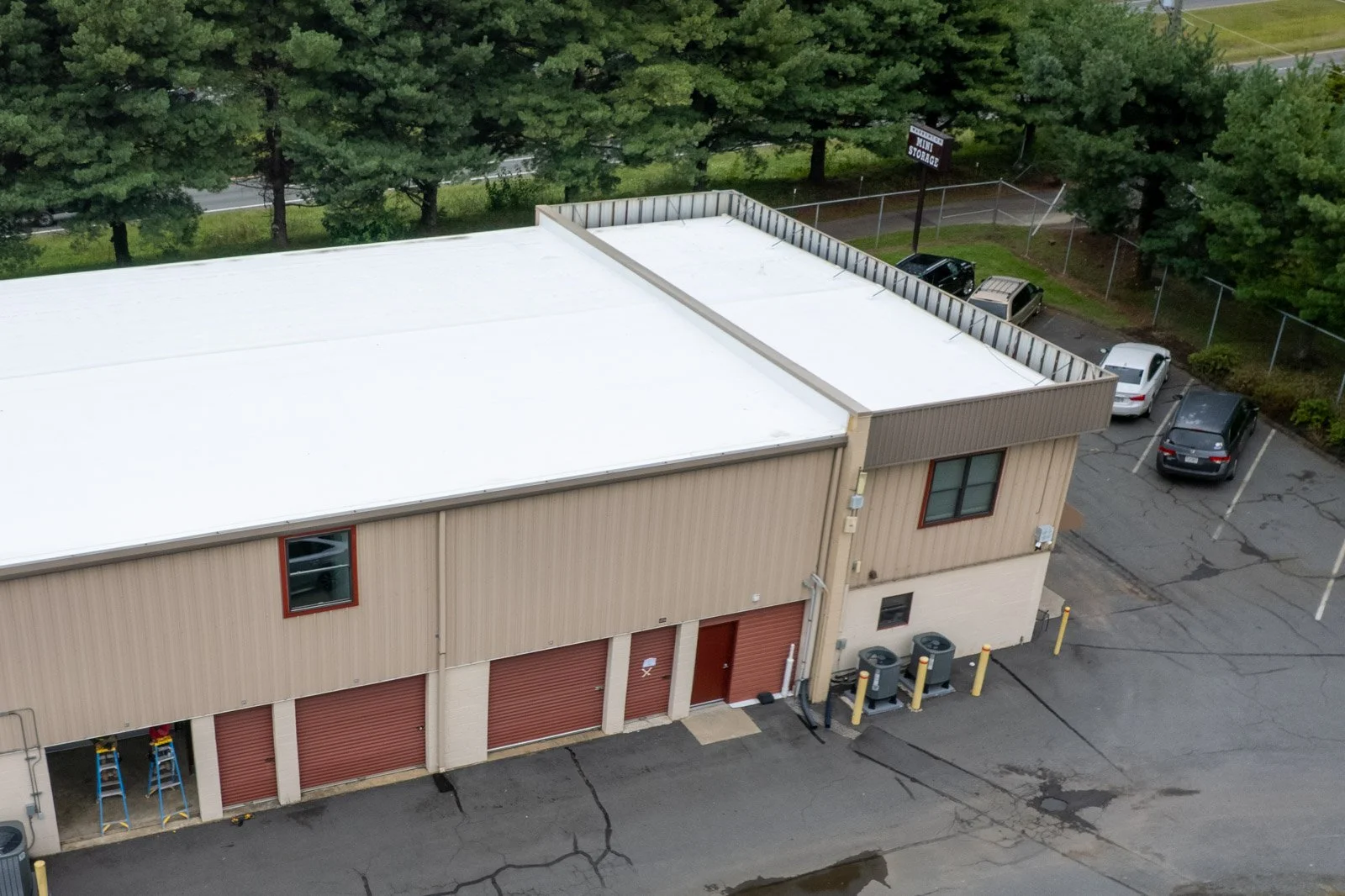 Close aerial view of the white TPO retrofit roof and raised office roof perimeter above red storage doors at Warrenton Mini Storage.