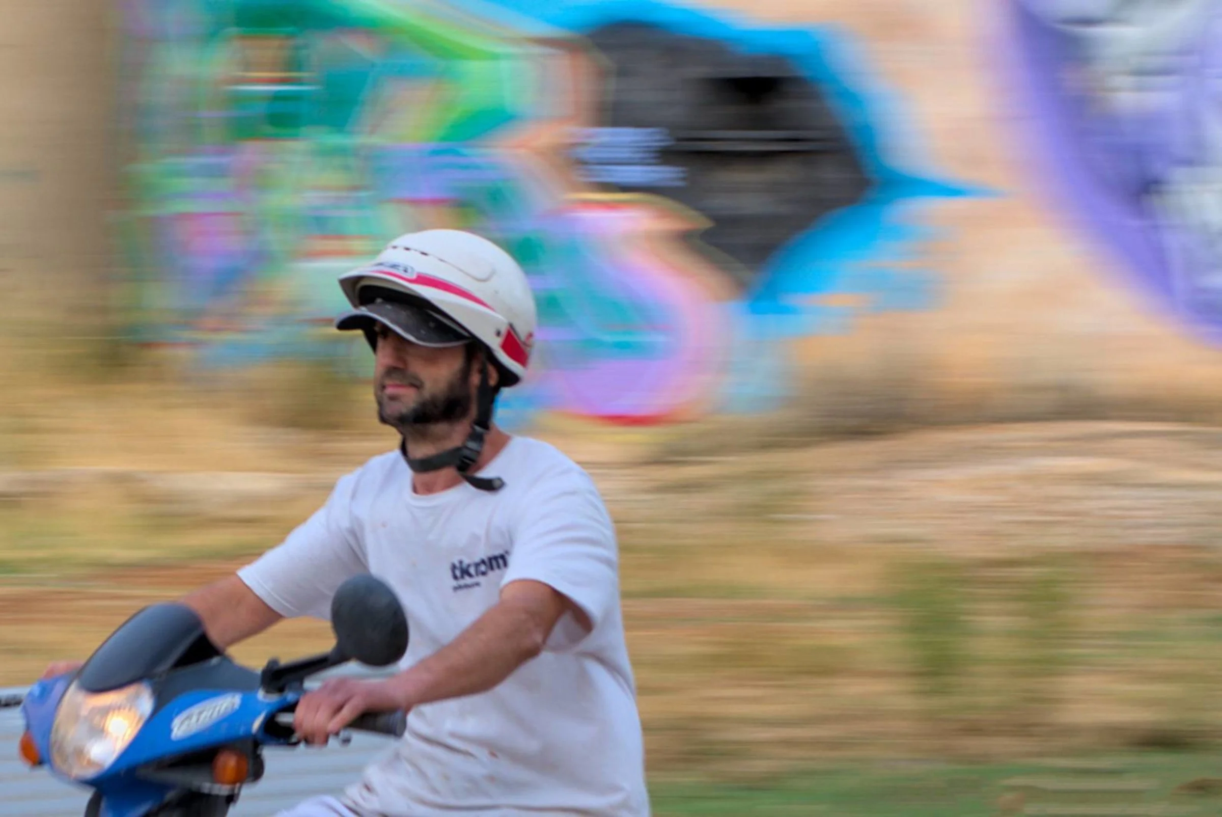 Painter riding a moped in front of colorful graffiti, motion blurred background.