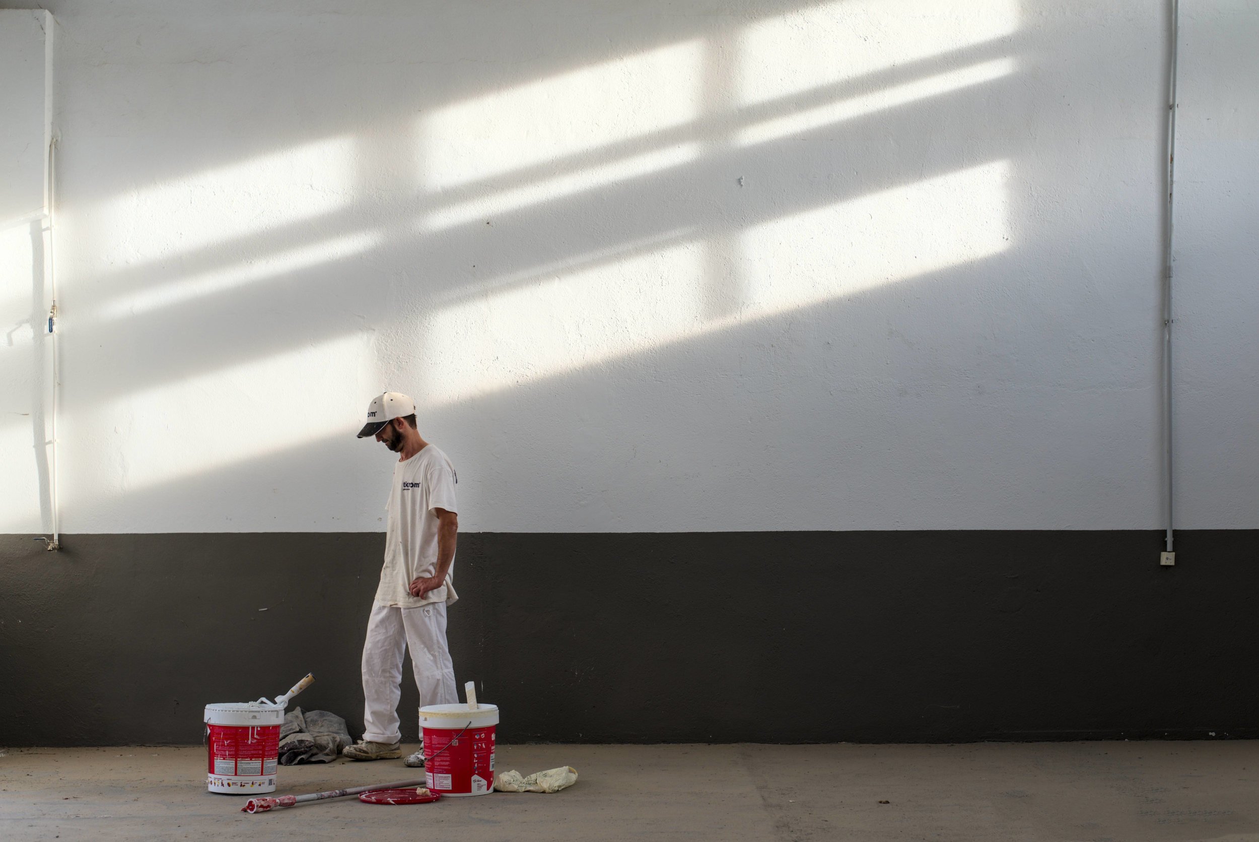 Painter standing in a large warehouse with dramatic diagonal light across the wall.