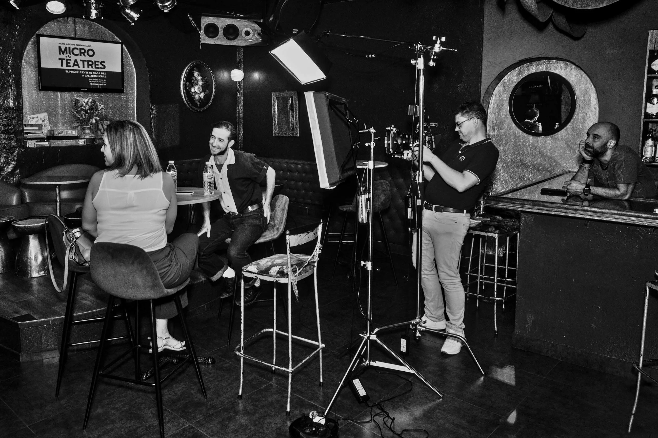 Film crew and cast gathered in a bar, lights and grip gear around them.