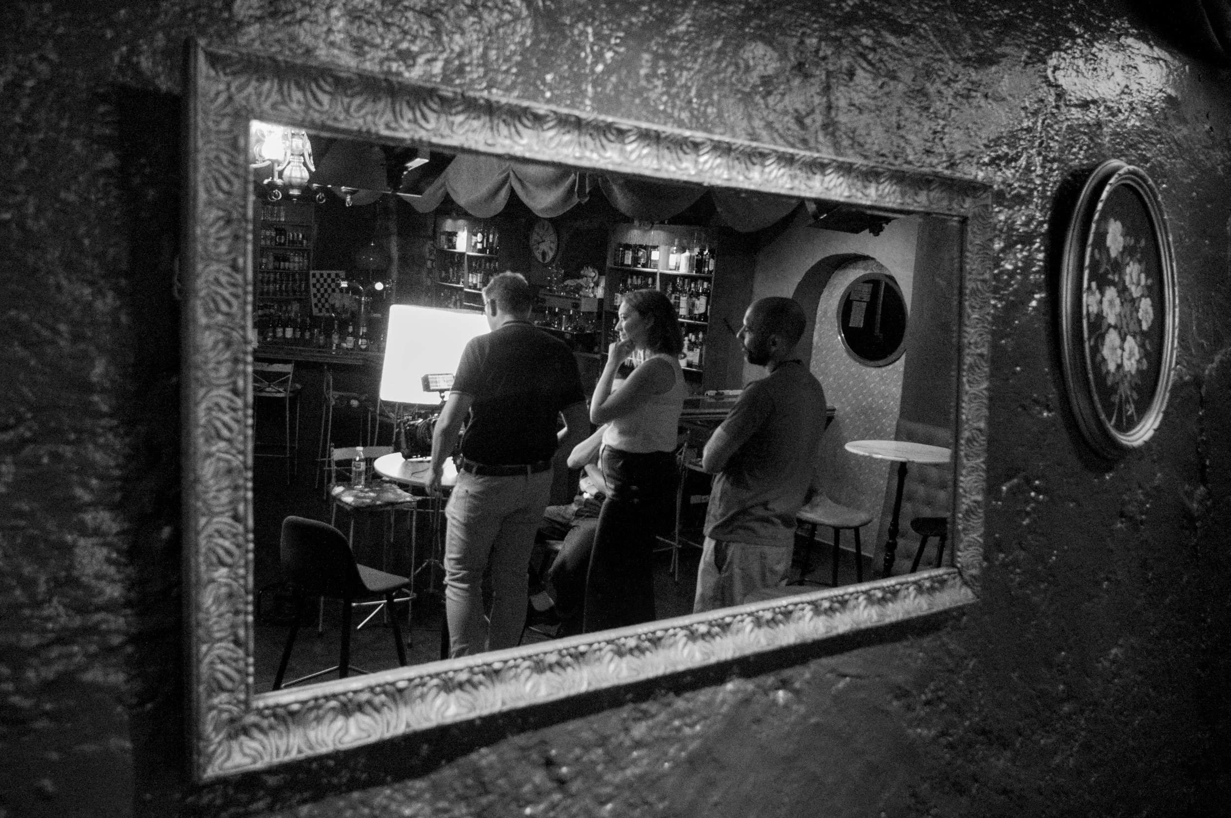 Reflection of the crew and bar set in a wall mirror, lights glowing.