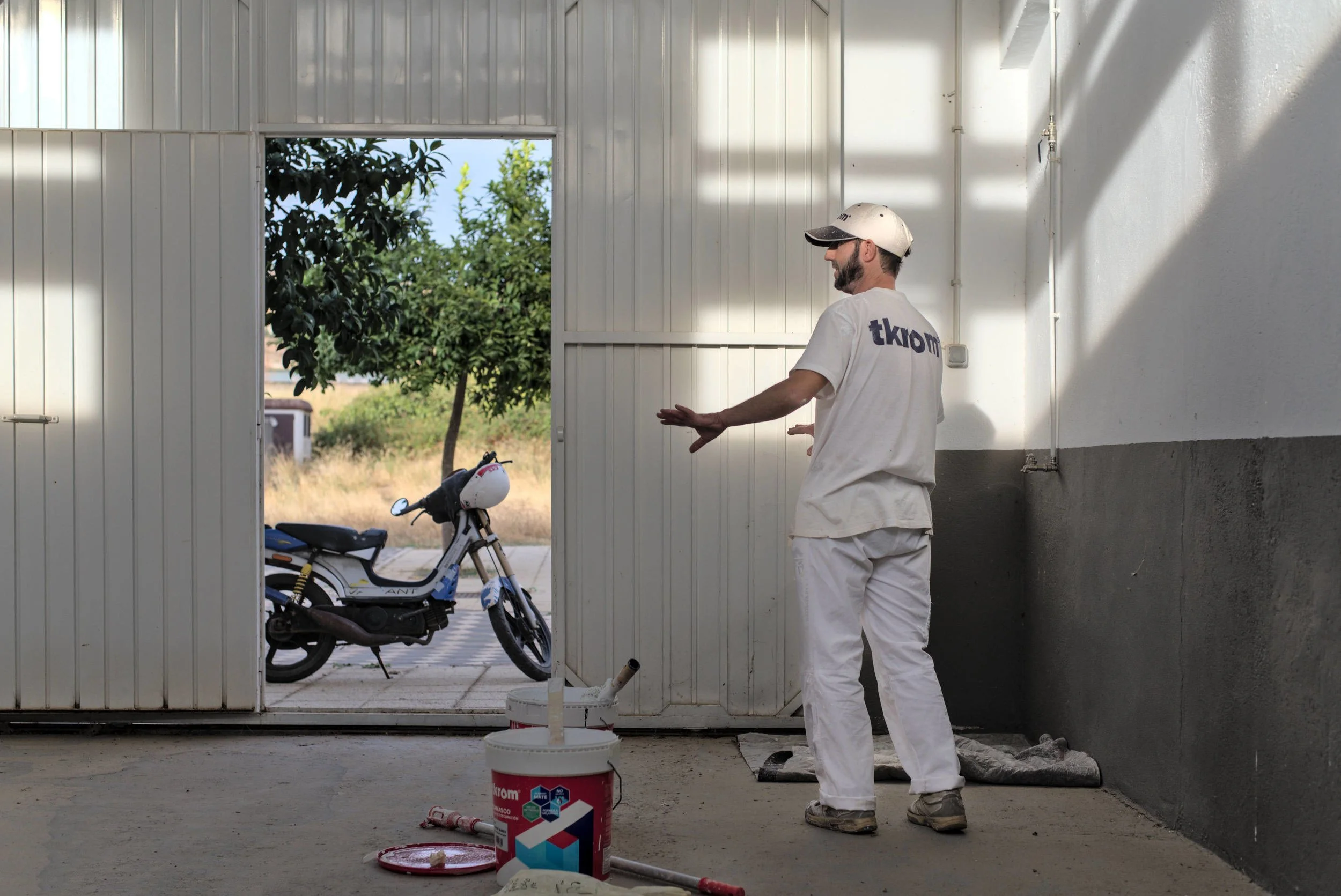 Painter standing by open warehouse door with moped visible outside.