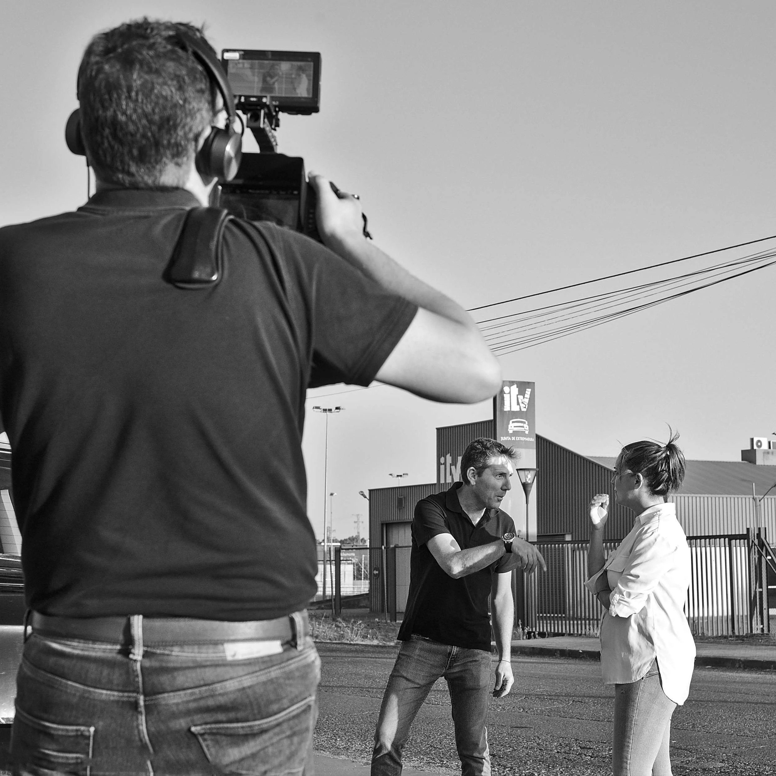 Cameraman filming two actors arguing beside an industrial ITV building.