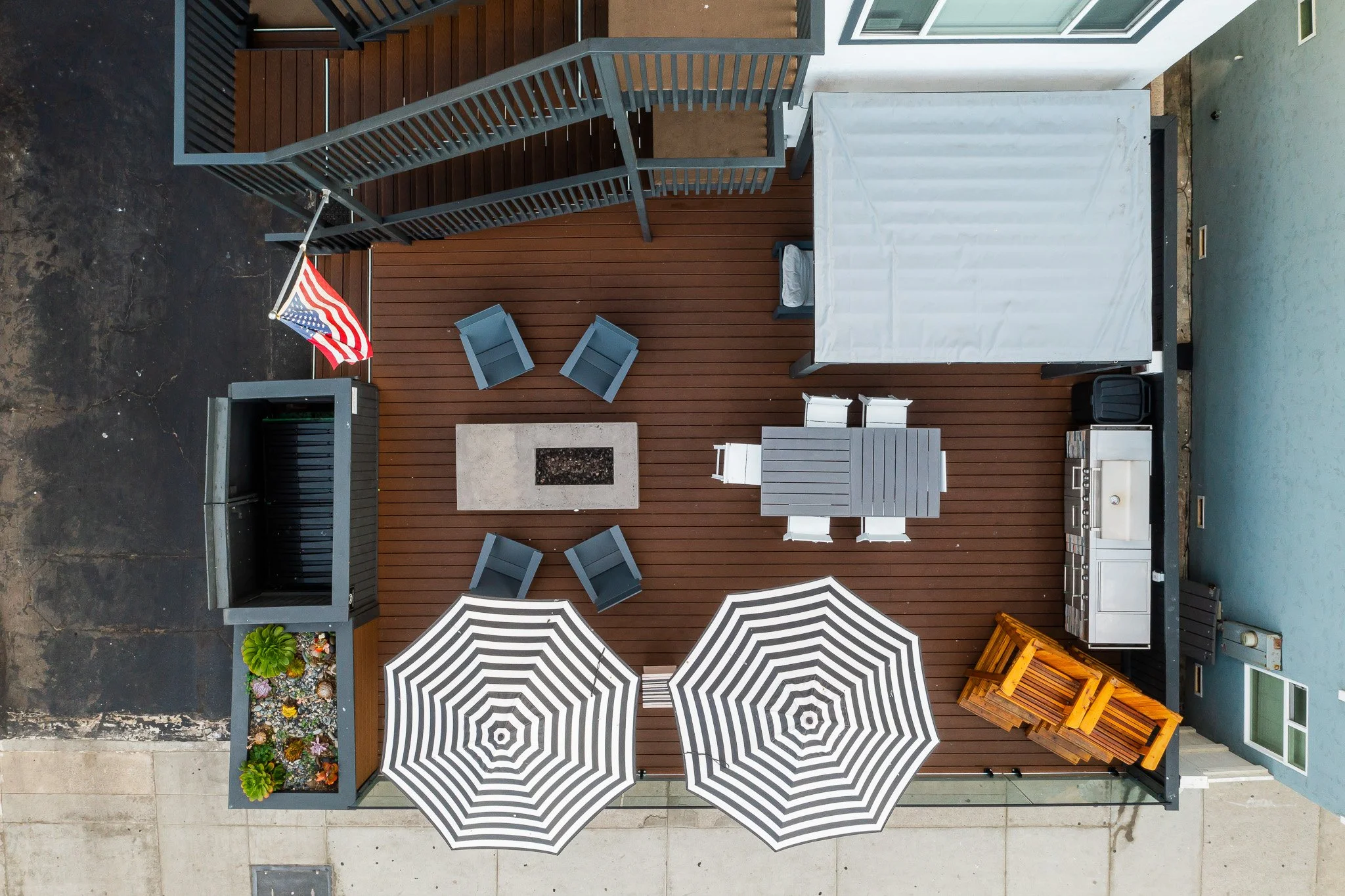 2-Bedroom Vacation Rentals in Oceanside, CA - Marbella - A Birdseye View Shows A Rooftop Deck With A Central Fire Pit, Outdoor Dining Table, Lounge Chairs, And Striped Umbrellas.