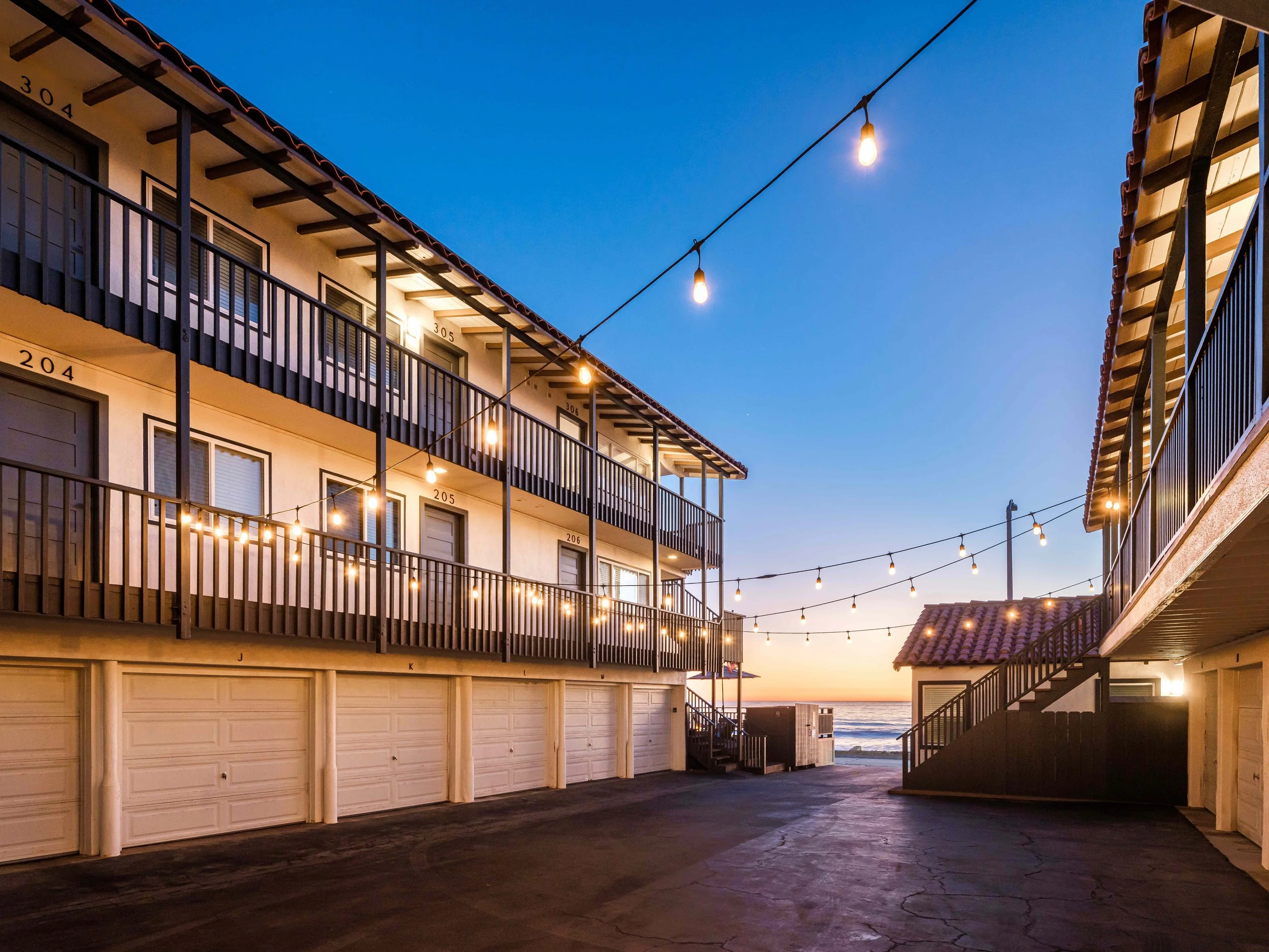 Studio Vacation Rentals In Oceanside, CA - Marbella - Property Parking Alley With Garages And Outdoor String Lights