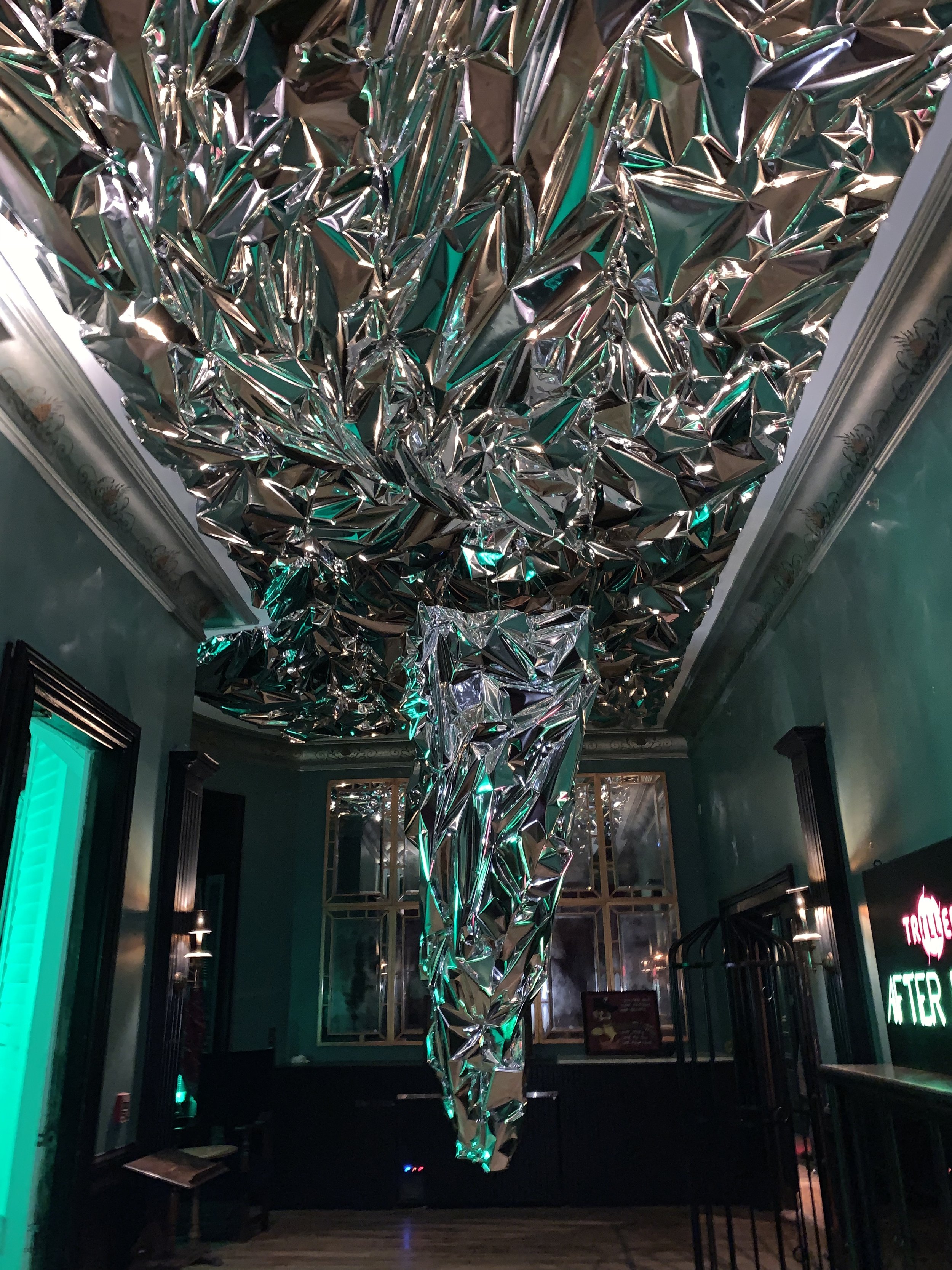 Room with metallic, reflective ceiling installation and teal lighting effect.