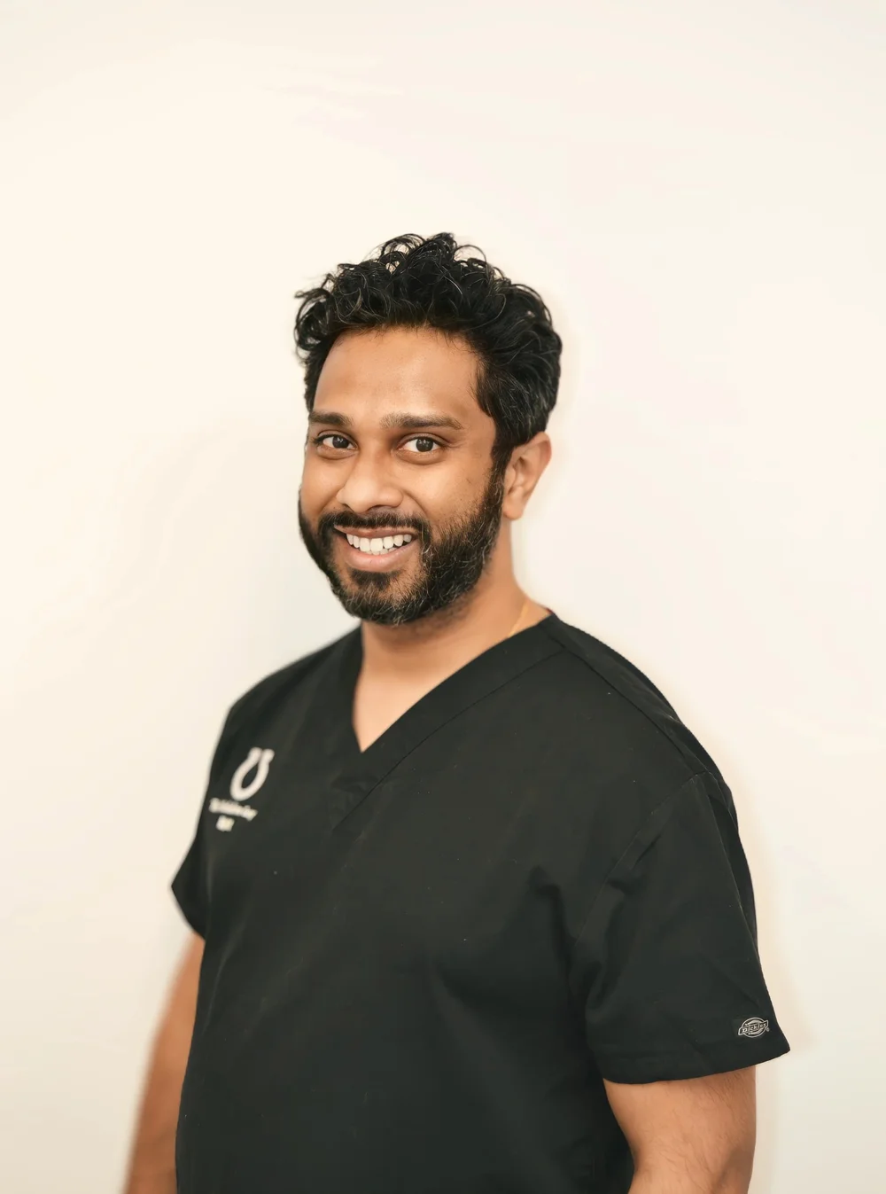 Matt Manikam, our implant dentist, in black scrubs at the practice