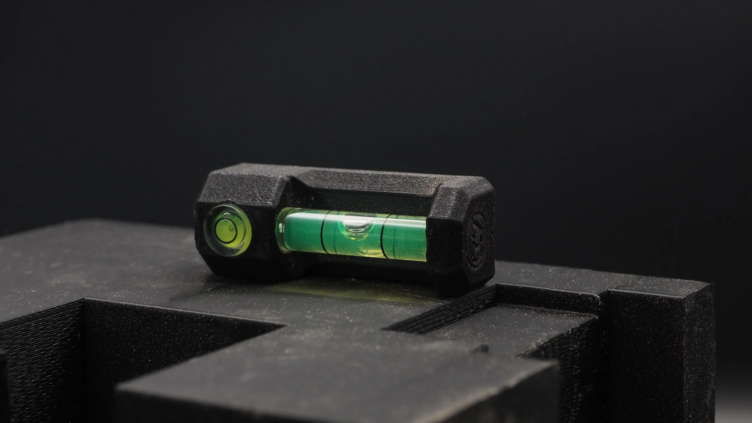 A Maker level resting on a black surface with a black foam-lined case beneath it.
