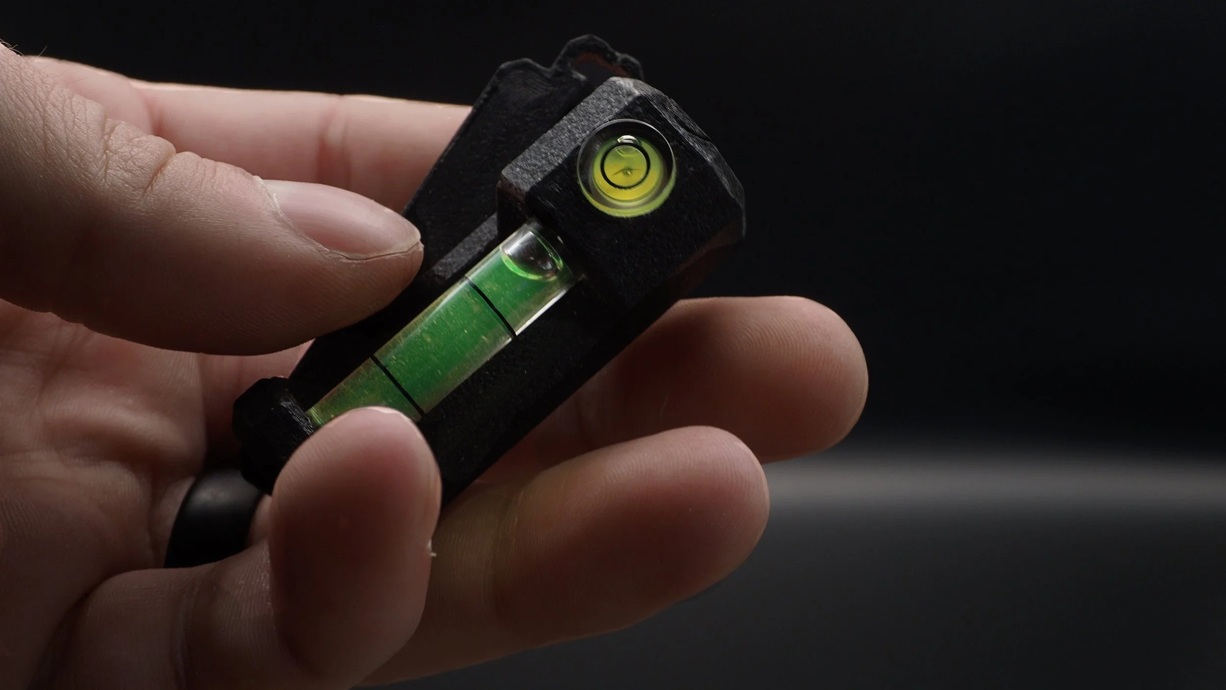 Close-up of a hand holding a small black device with a horizontal bubble level and a spirit level, used for measuring or leveling.