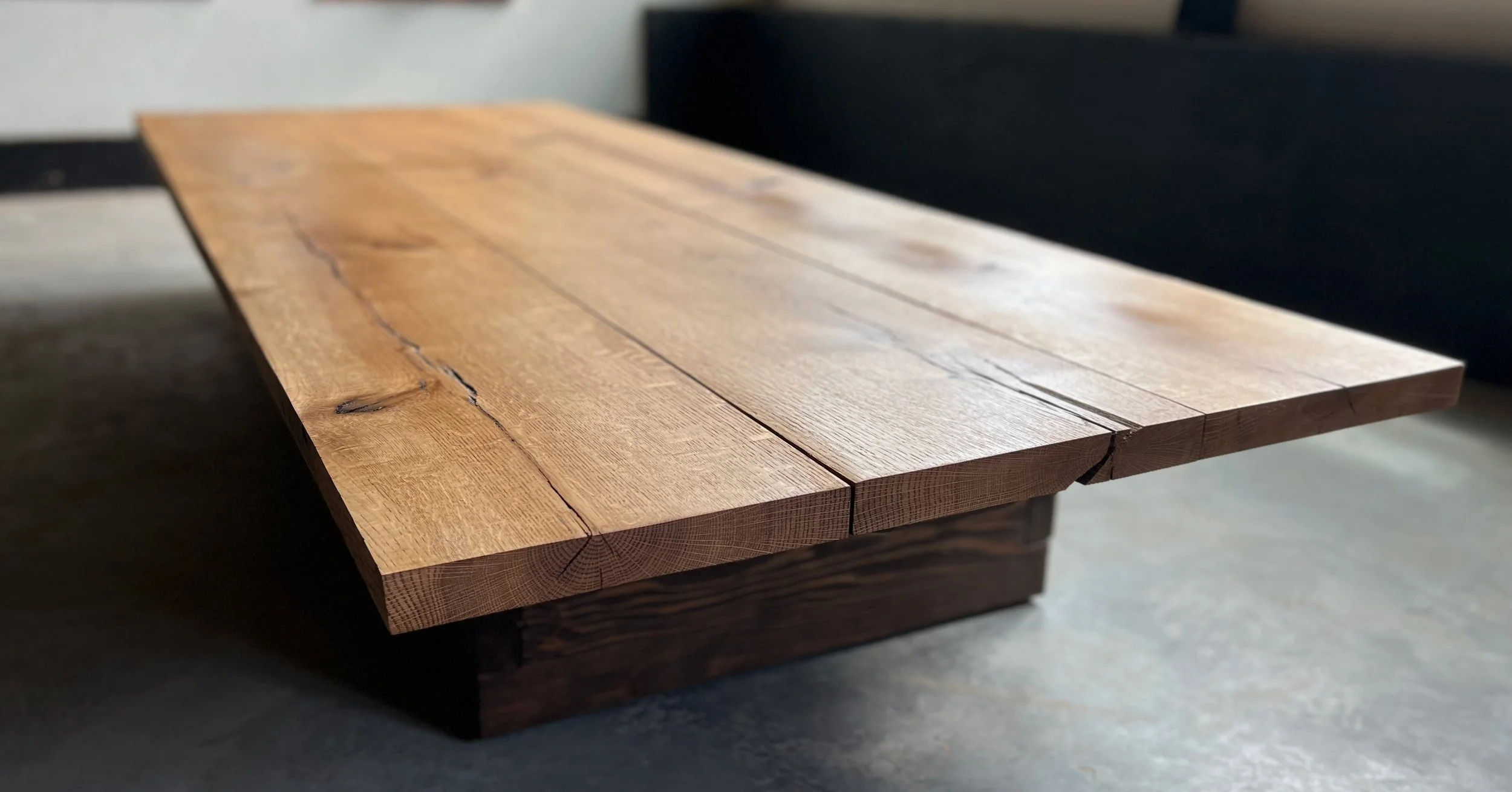 Close-up of a wooden table with a smooth, polished surface and visible wood grain, set on a darker base.