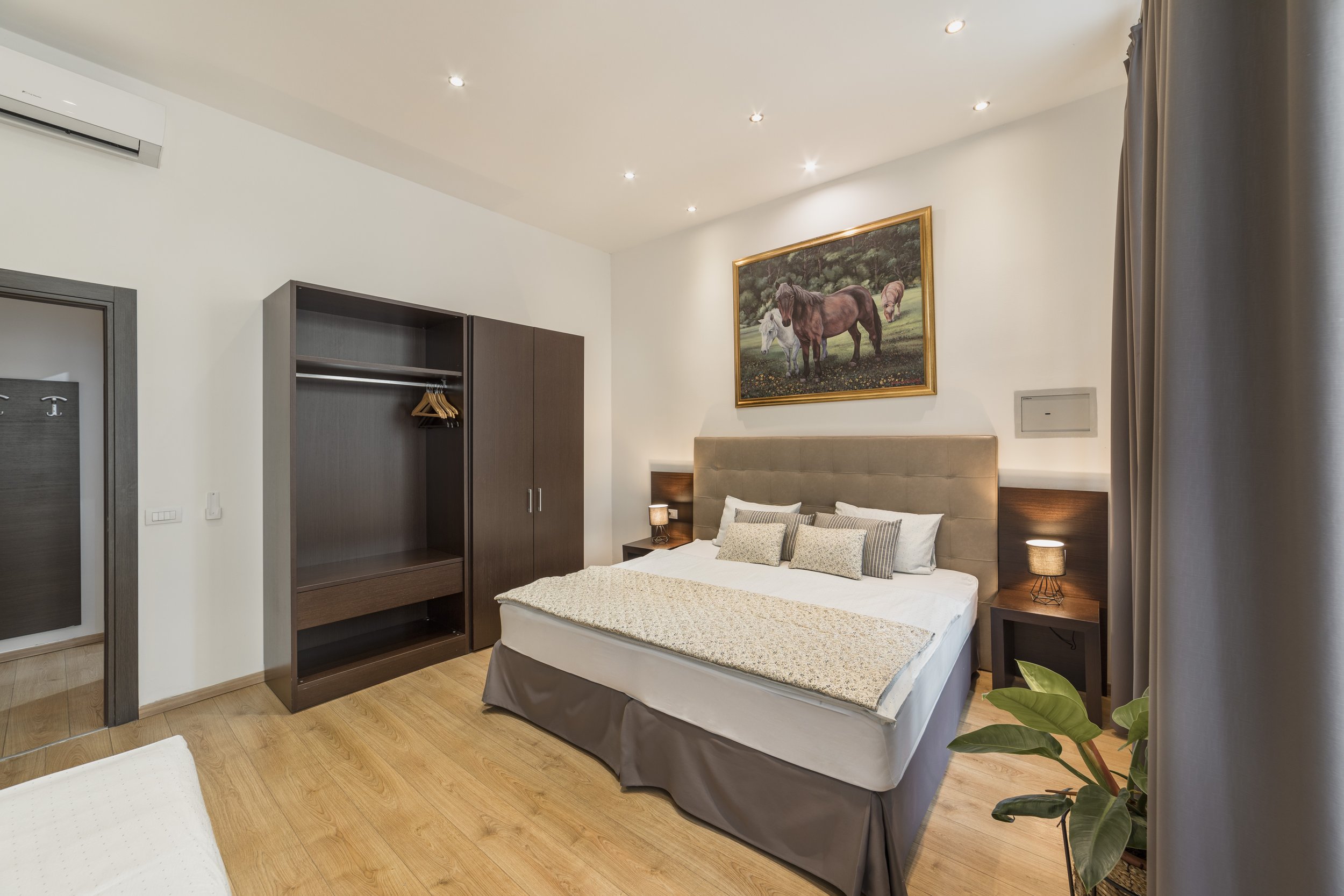 A hotel room with a bed, nightstands, artwork of horses on the wall, and a closet.