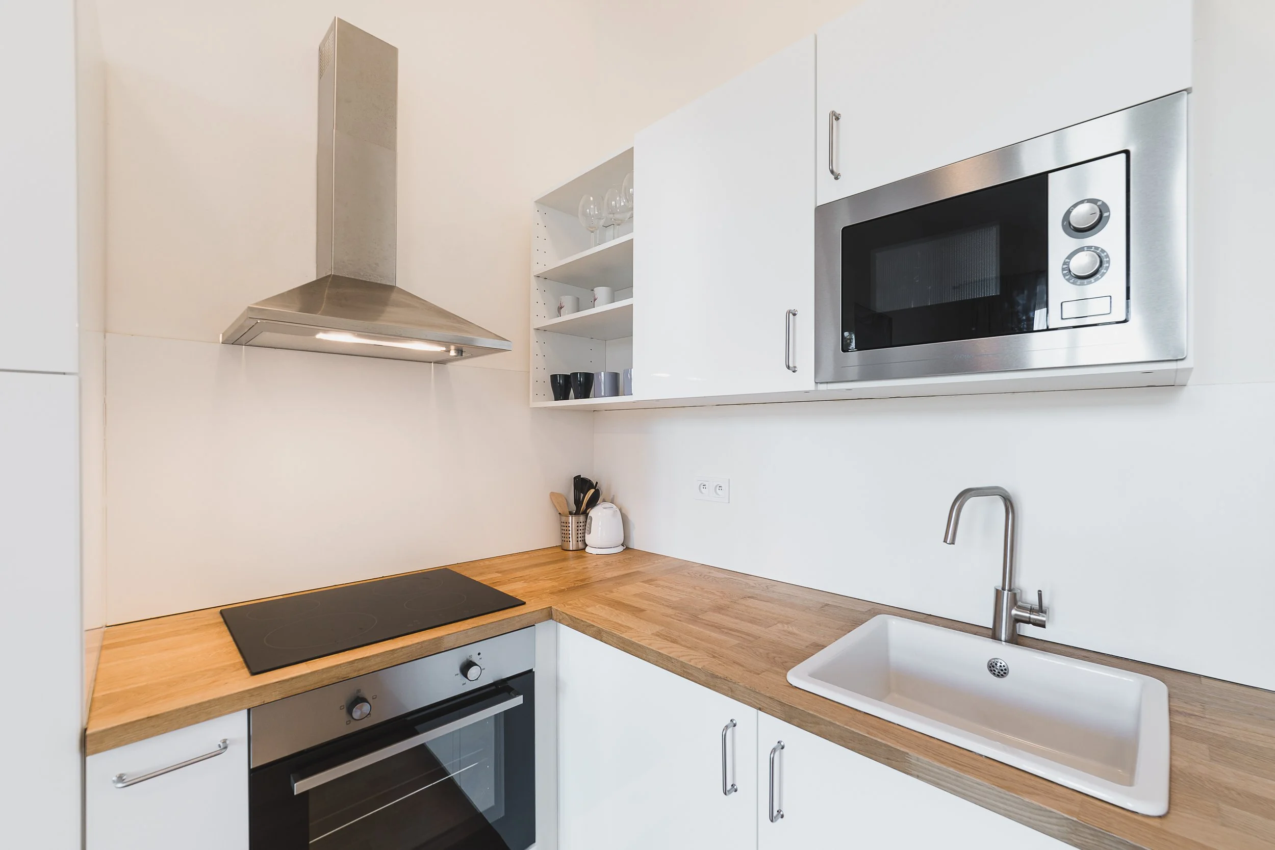 Modern kitchen with white cabinets, wooden countertop, microwave, stovetop, oven, and sink, with a few kitchen items on the counter.