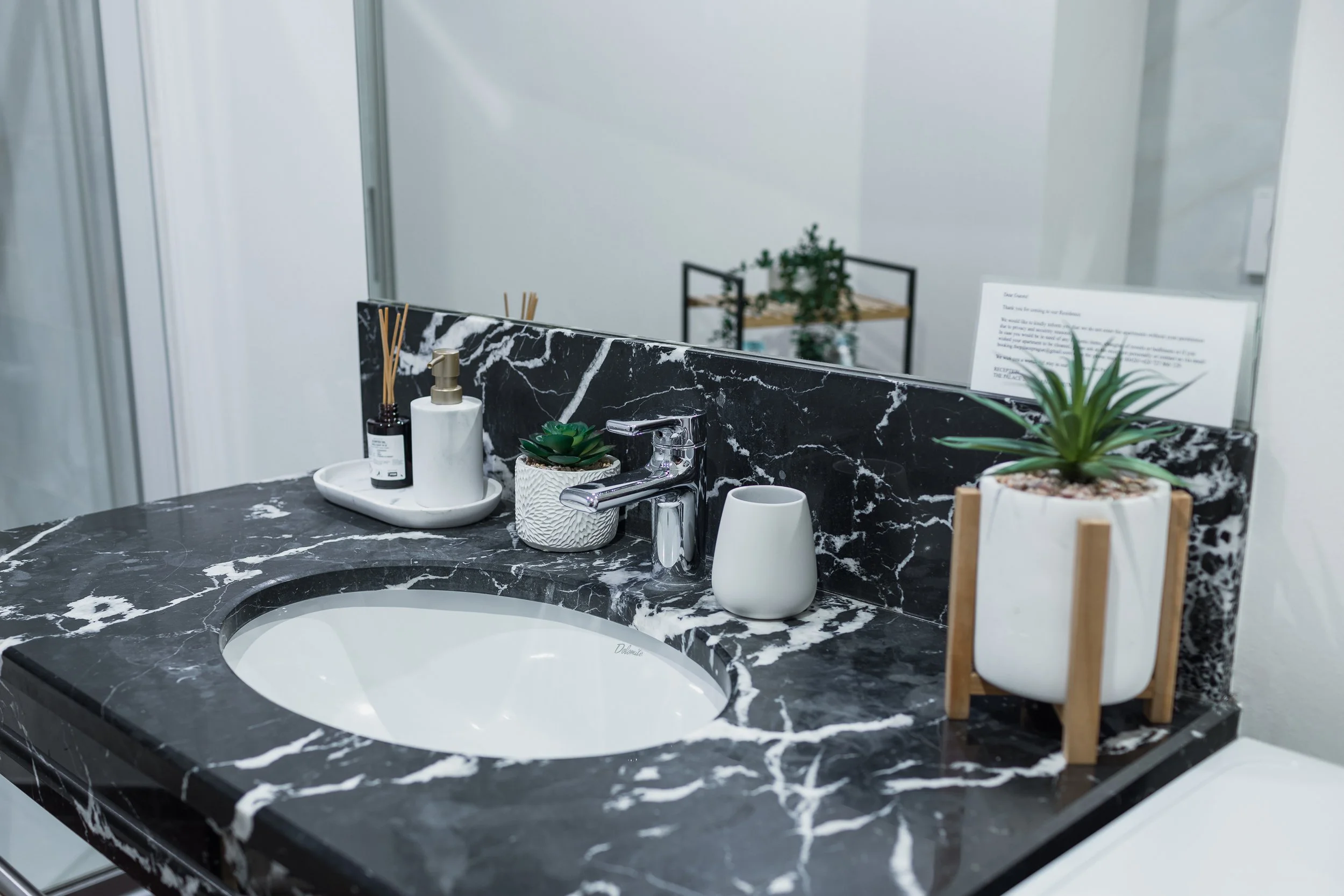 Bathroom vanity with a black marble countertop, a white oval sink, and various toiletries and plants on the counter.