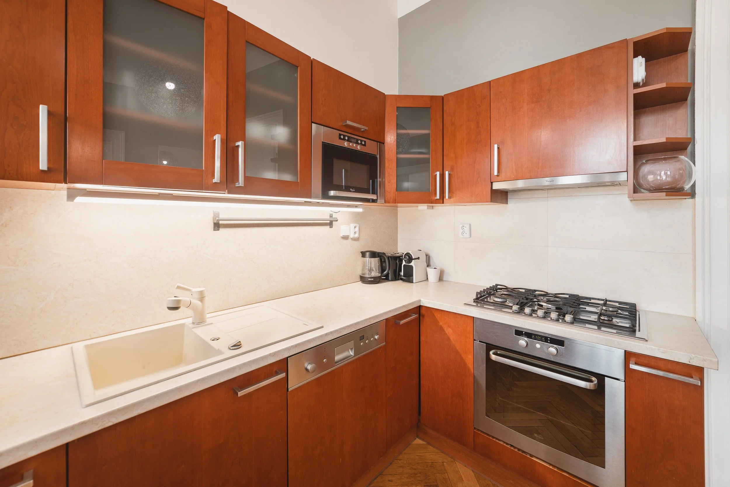 Kitchen with wooden cabinets, cream countertop, built-in microwave, gas stove, coffee maker, and a glass bowl on a small shelf.