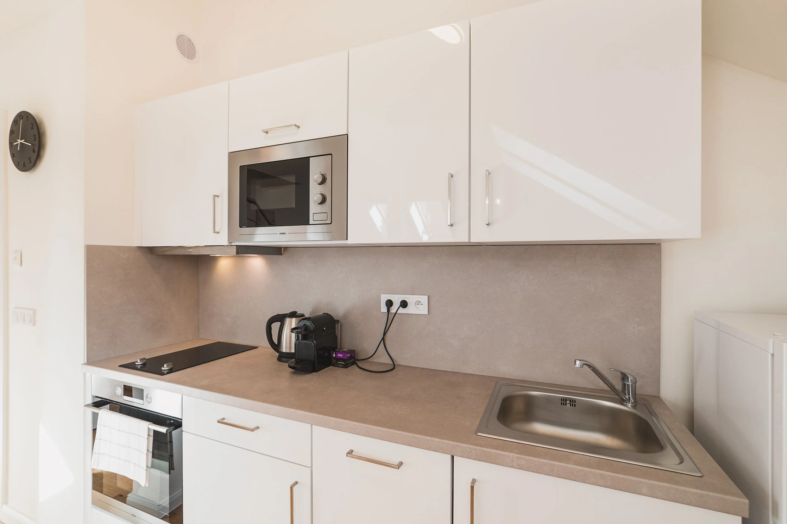 Modern kitchen with white cabinets, beige countertop, built-in microwave, electric stove, stainless steel sink, and minimal decor.