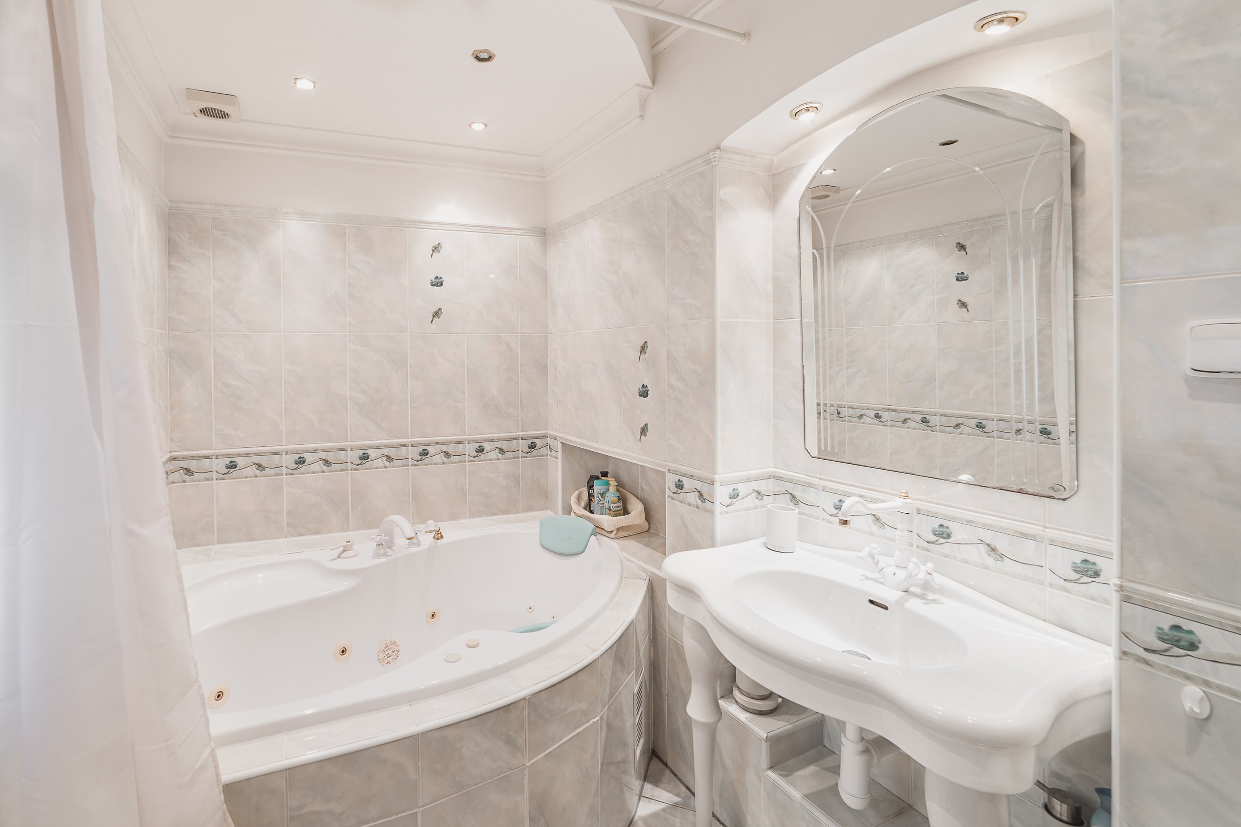 Bathroom with bathtub, sink, mirror, and tiled walls and ceiling.