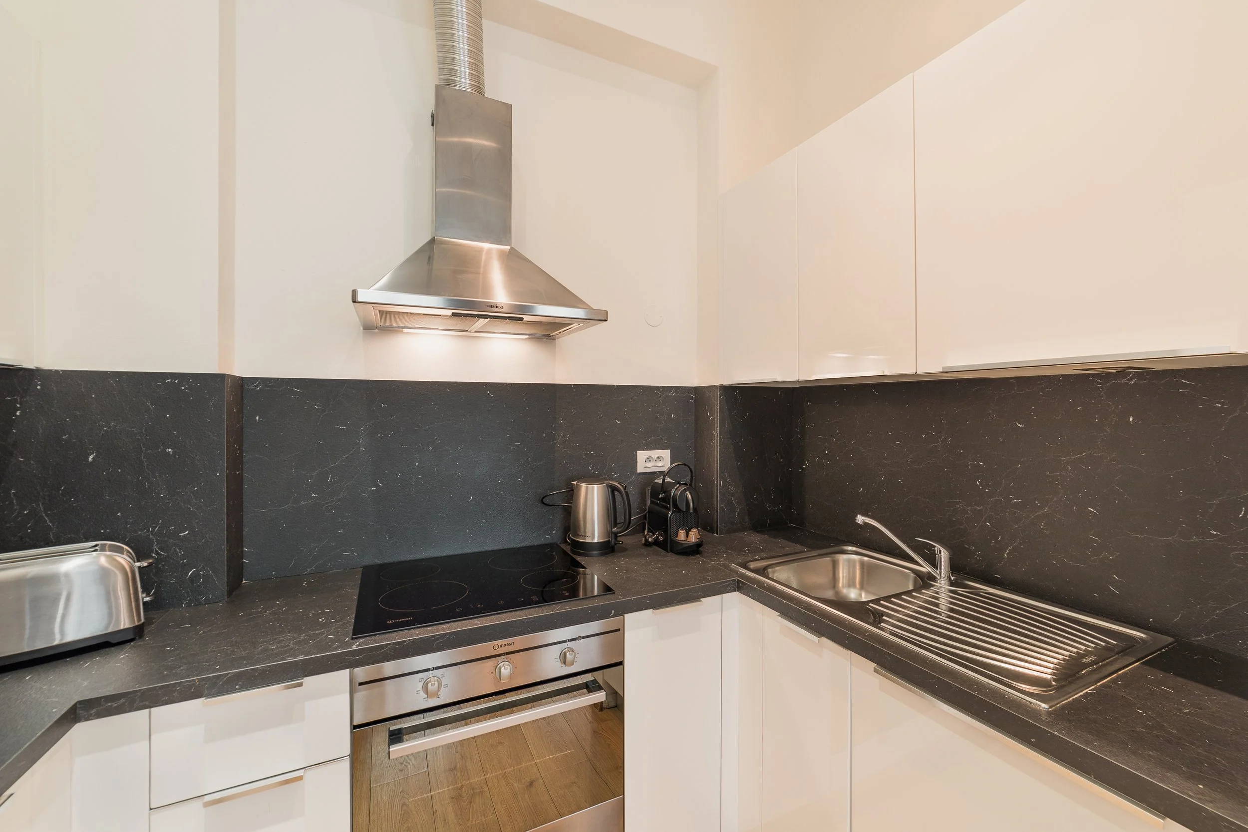 Modern kitchen with black marble countertops, white cabinets, and stainless steel appliances including a stove, oven, kettle, and range hood.