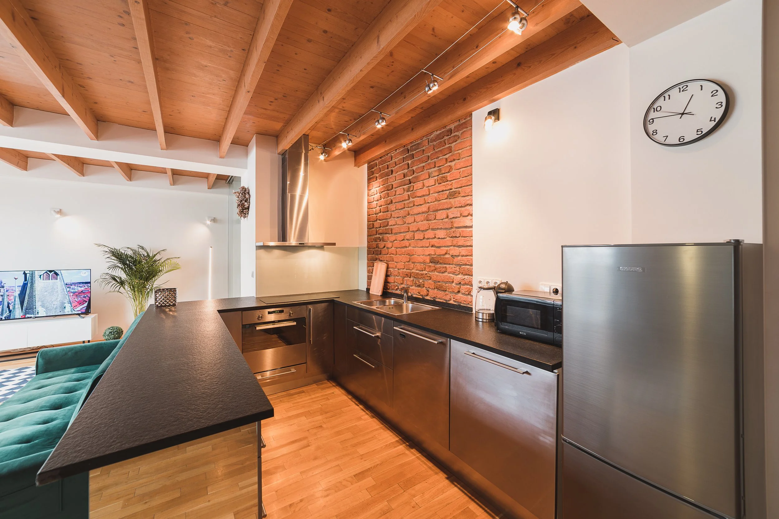 Modern kitchen with wood ceiling, brick wall, stainless steel appliances, black countertop, and a wall clock showing 10:08.