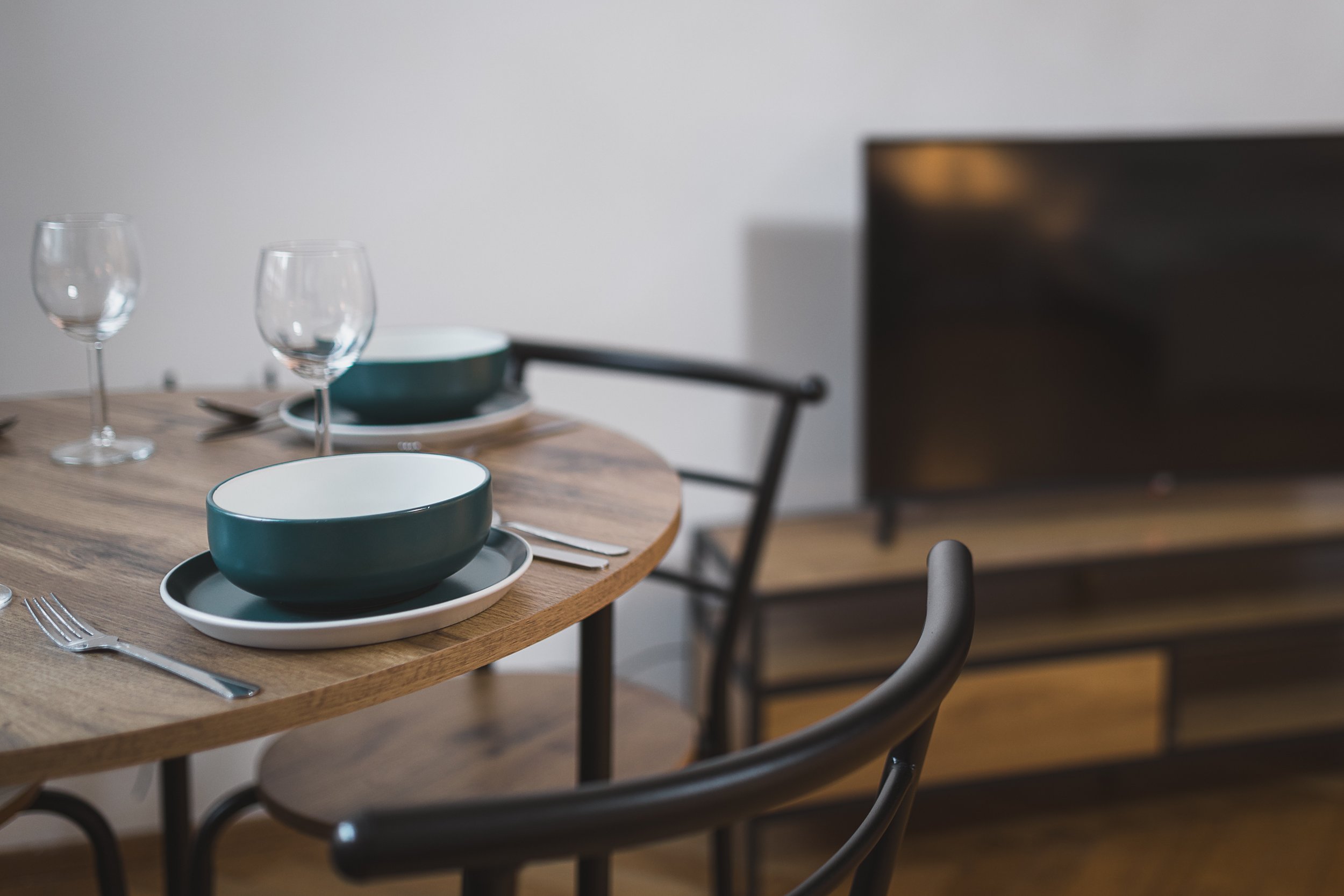 A dining table set with two empty wine glasses, two bowls on plates, and silverware in a modern, minimalist dining area.
