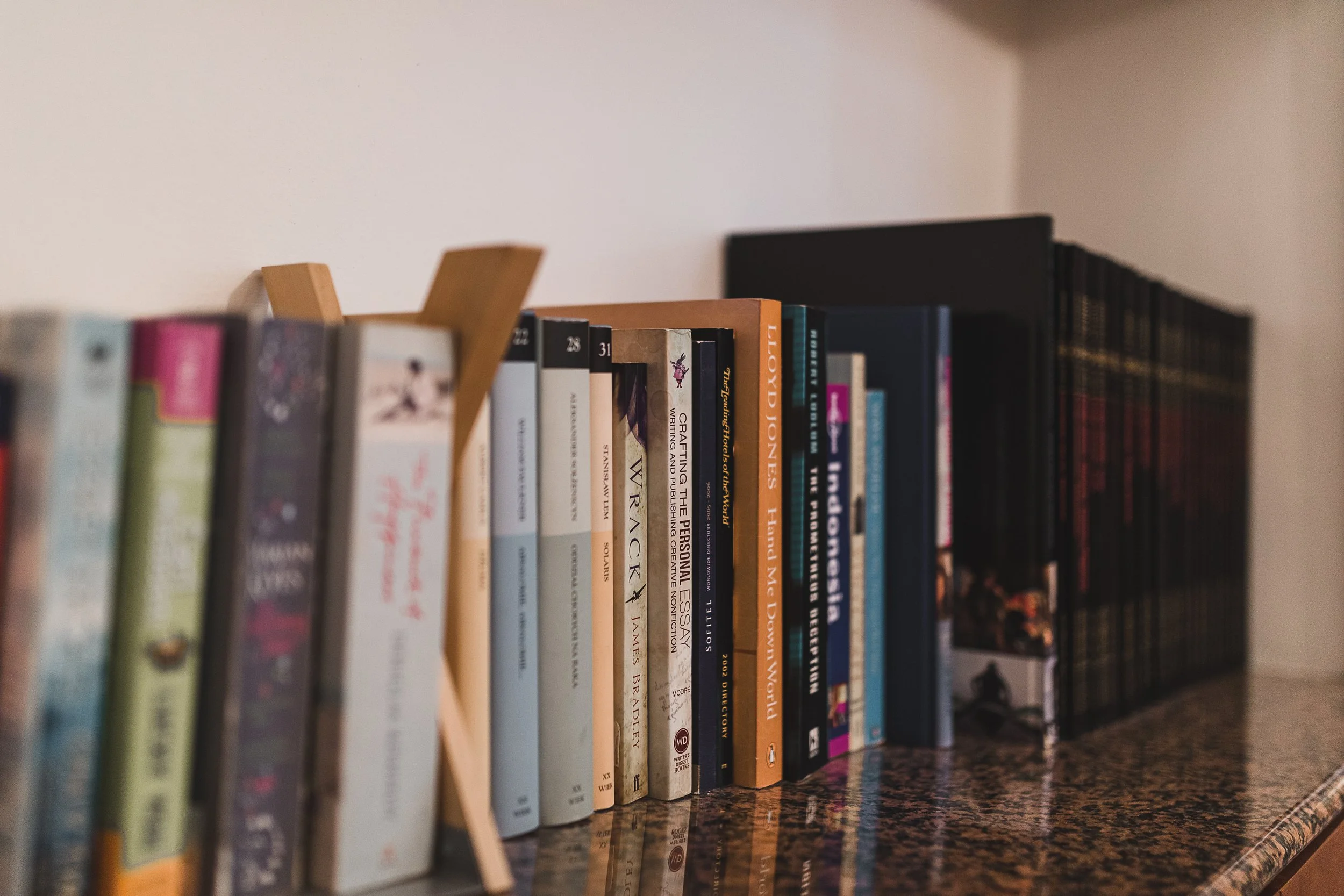 Close-up of a bookshelf with various books arranged vertically on a speckled countertop.