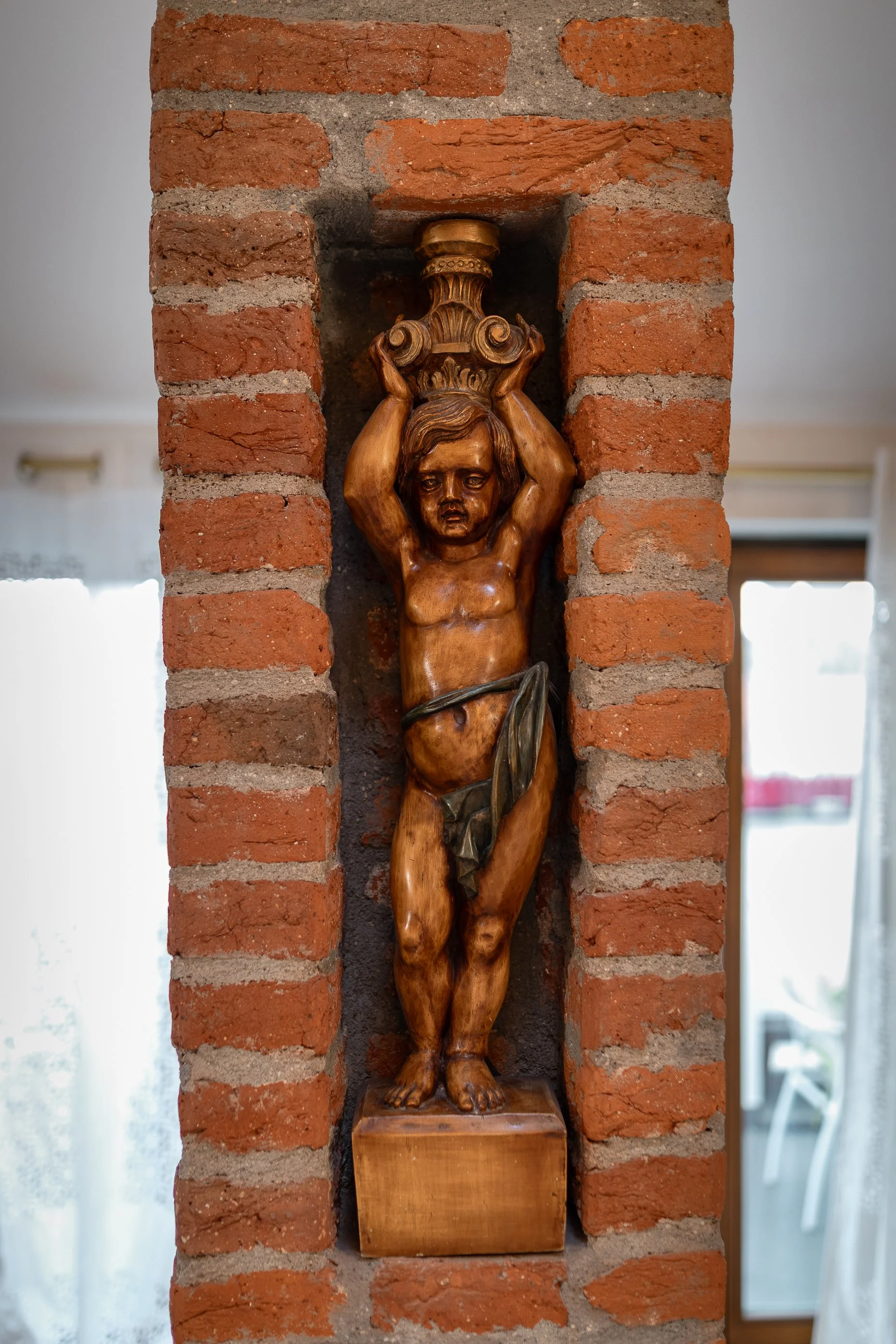 A wooden sculpture of Jesus Christ on a cross, mounted on a brick wall.