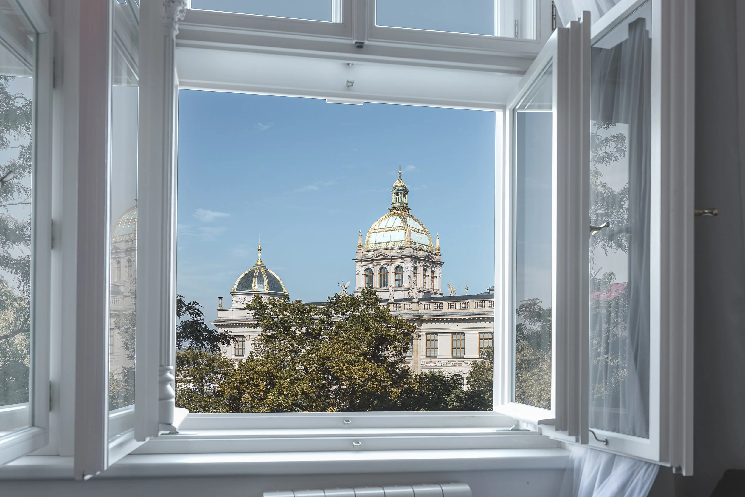 View of a historic building with a gold-domed roof seen through an open window in a bright, airy room.