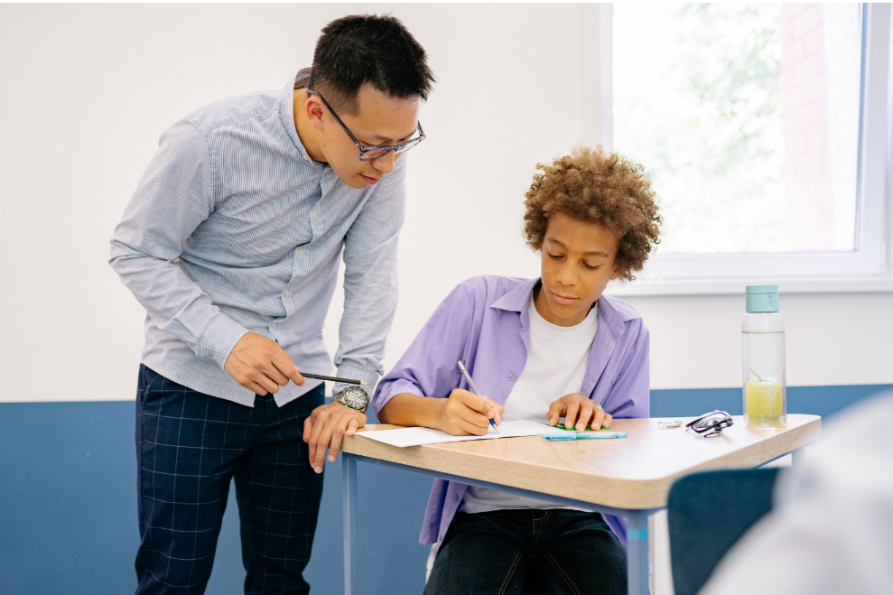 teacher working with a student who is handwriting on paper