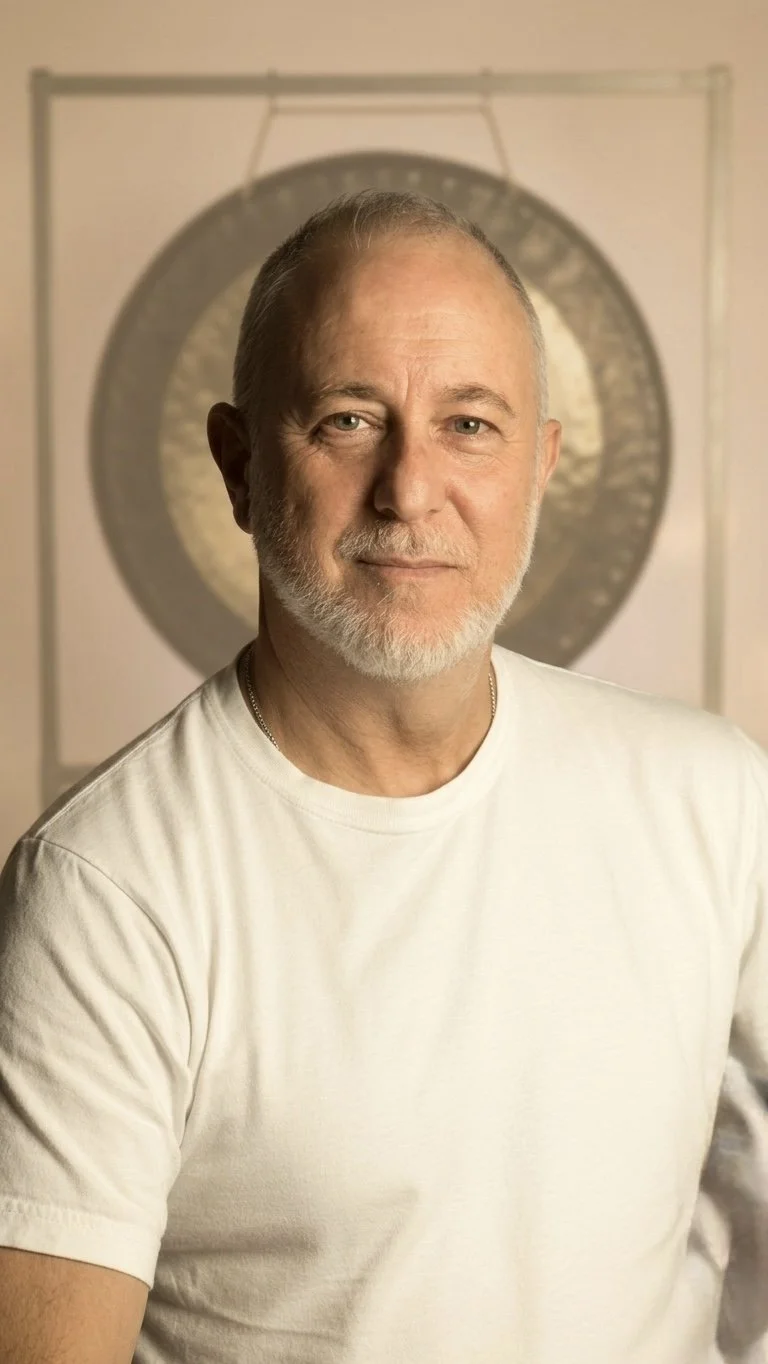 A middle-aged man with a beard and short hair standing in front of a circular gong.
