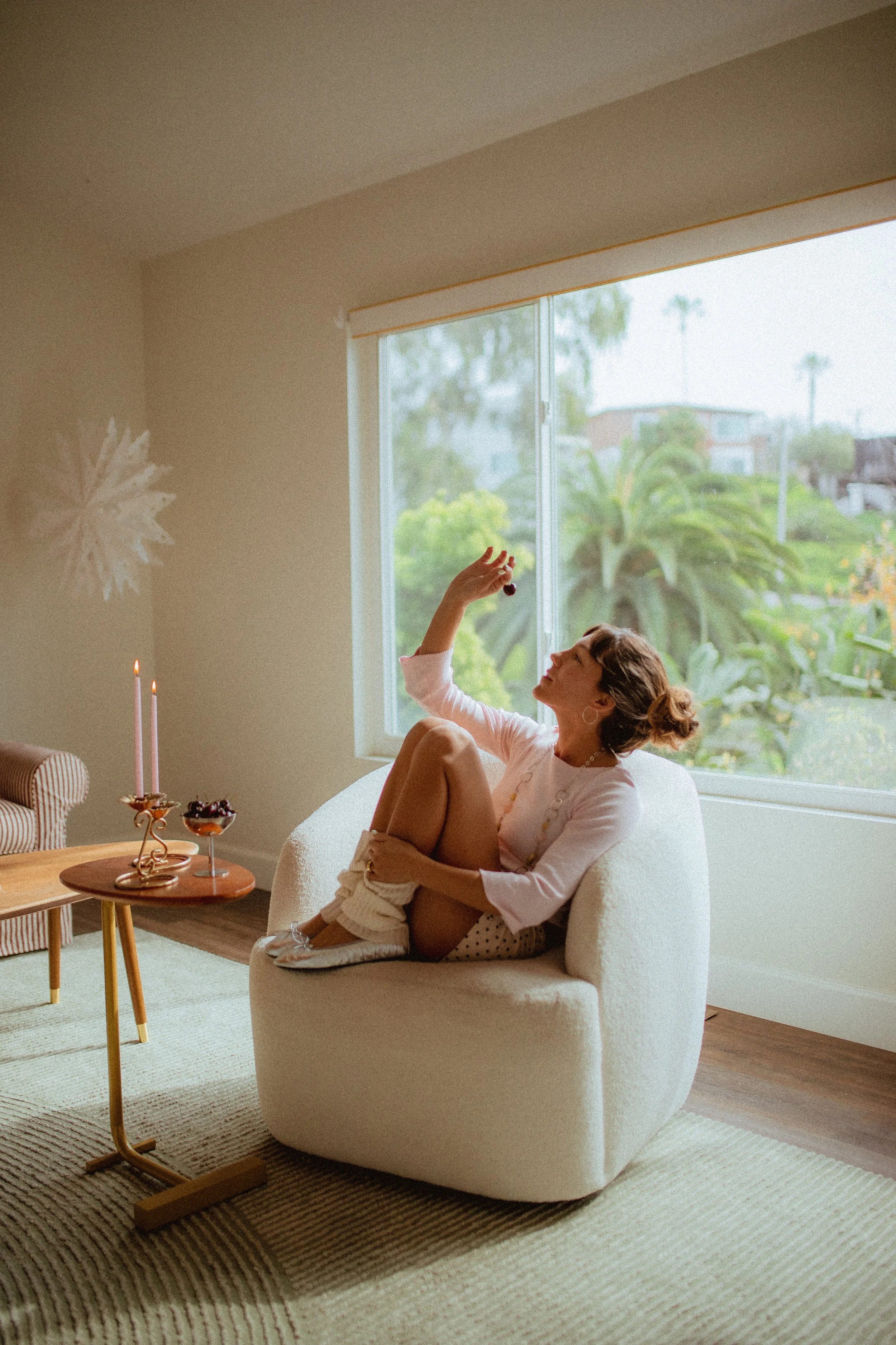 chrome glass full of dark cherries sitting on a red striped couch, Aestehtic cherry lifestyle photoshoot, Chloe Monotoya in her home in San Clemente, Cute girly aesthetic, pink candlesticks, white bubble chair, leg warmers, micro shorts and ballet fl
