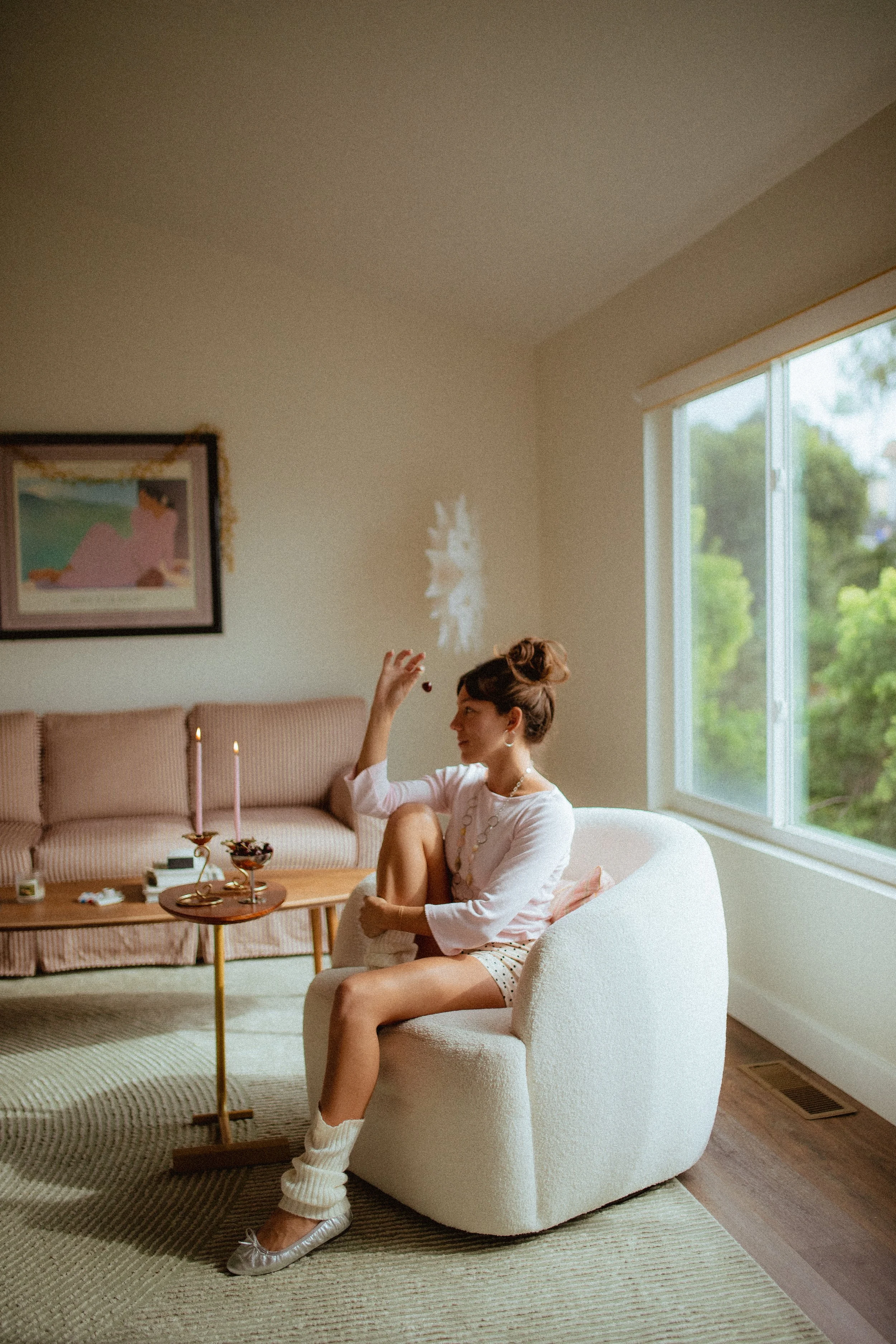 chrome glass full of dark cherries sitting on a red striped couch, Aestehtic cherry lifestyle photoshoot, Chloe Monotoya in her home in San Clemente, Cute girly aesthetic, pink candlesticks, white bubble chair, leg warmers, micro shorts and ballet fl