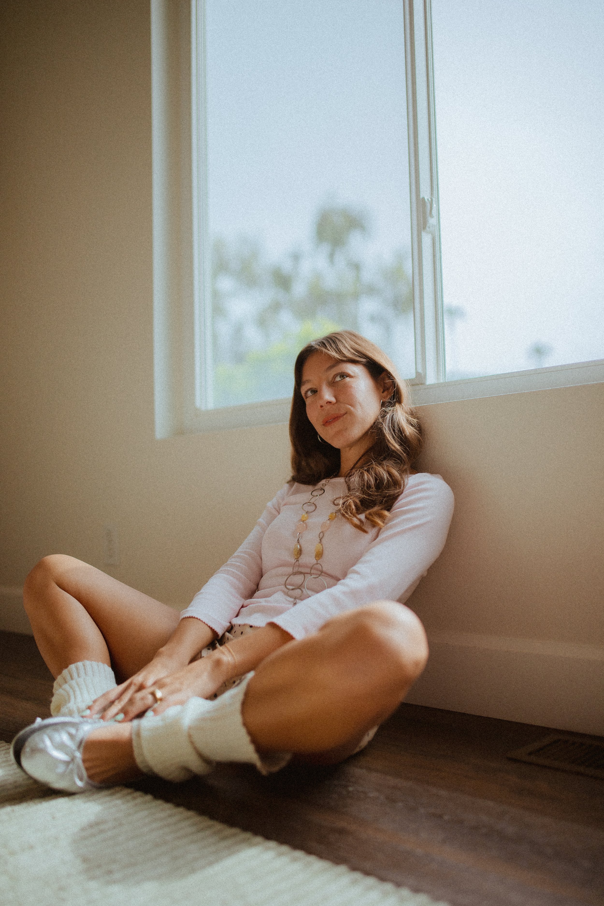 Chloe Montoya sitting on groudn posing in her home in San clemente, CA. Photo taken by southern california lifestyle creative portrait photographer- KElsie Carlson. Model sitting by window, posing inspiration, girly fem outfit inspiration