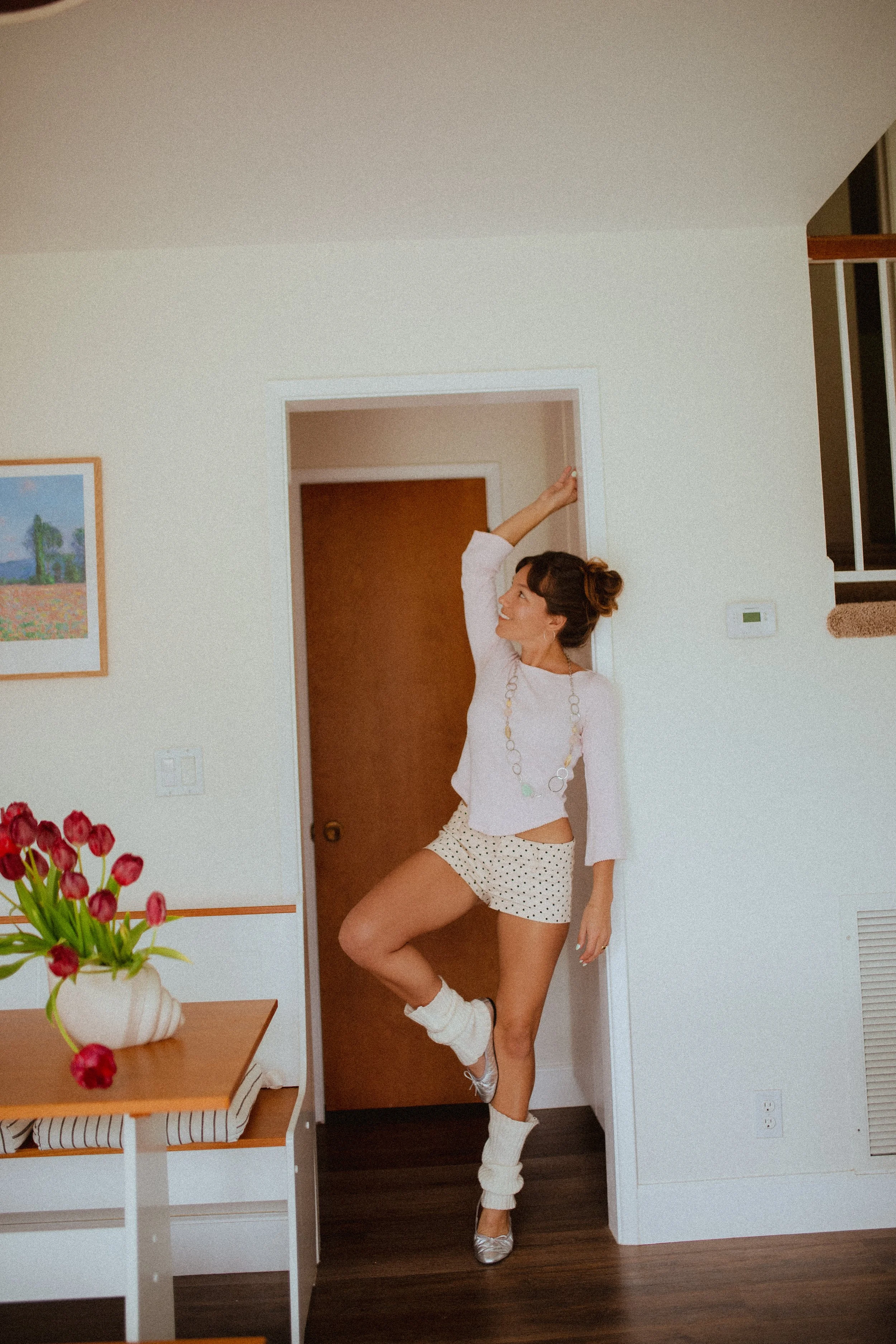 Chloe Montoya standing in her doorway in her home in orange county, CA. Creative lifestyle portrait photoshoot- standing ina. fun and unique way in home photoshoot, Wearing, Ballet flats, leg warmers and micro shorts. POsing inspiration for creative 
