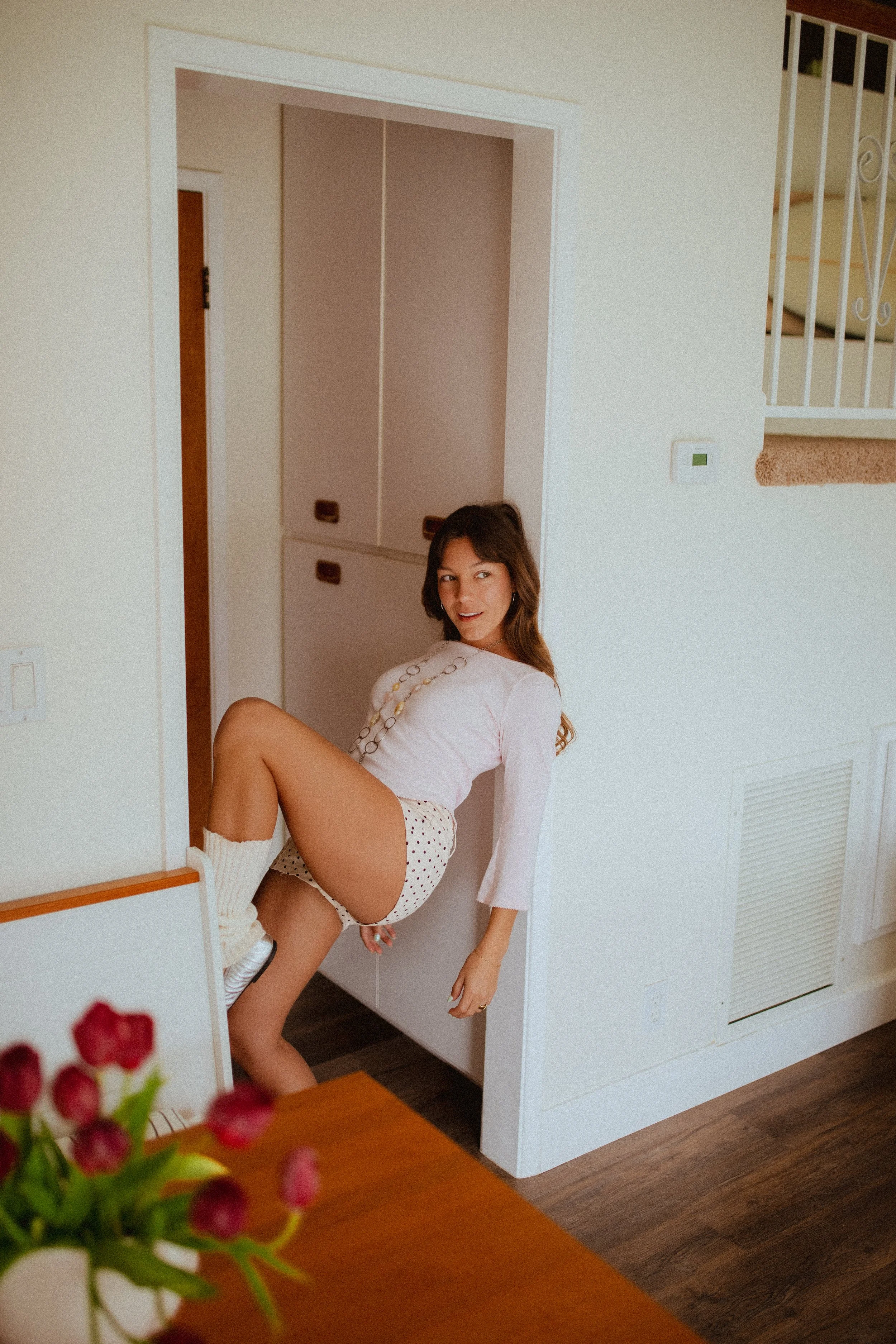 Chloe Montoya standing in her doorway in her home in orange county, CA. Creative lifestyle portrait photoshoot- standing ina. fun and unique way in home photoshoot, Wearing, Ballet flats, leg warmers and micro shorts. POsing inspiration for creative 