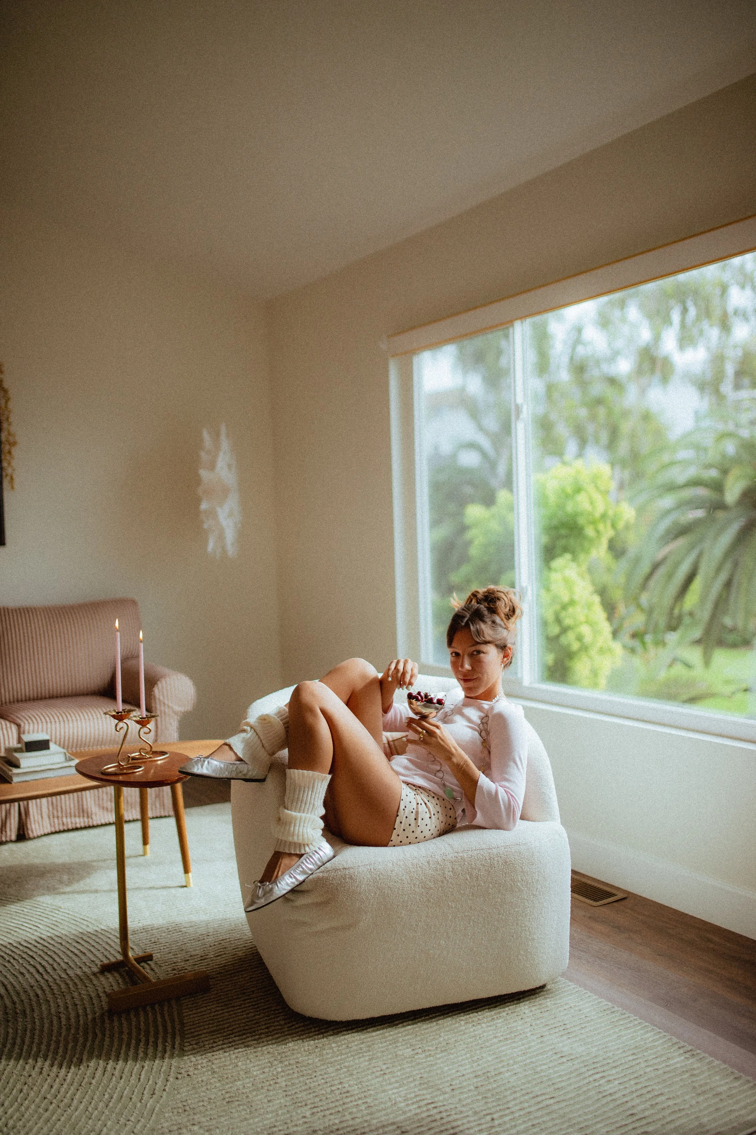 chrome glass full of dark cherries sitting on a red striped couch, Aestehtic cherry lifestyle photoshoot, Chloe Monotoya in her home in San Clemente, Cute girly aesthetic, pink candlesticks, white bubble chair, leg warmers, micro shorts and ballet fl