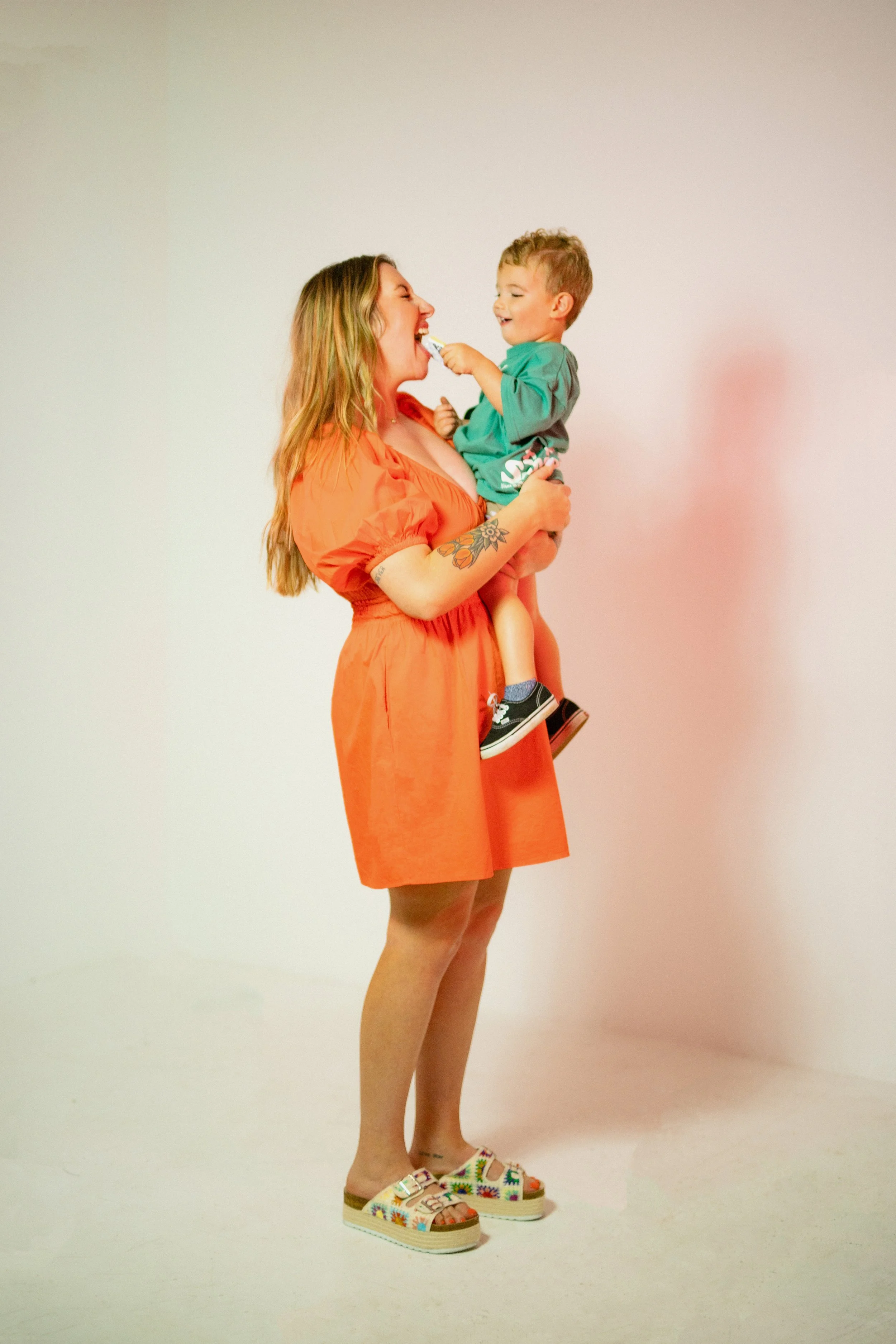 Southern California cookie decorator and home baker sitting on studio floor with her toddler, holding decorated sugar cookies during lifestyle branding session. Candid, personality-driven small business photography for creative mom entrepreneur. Capt