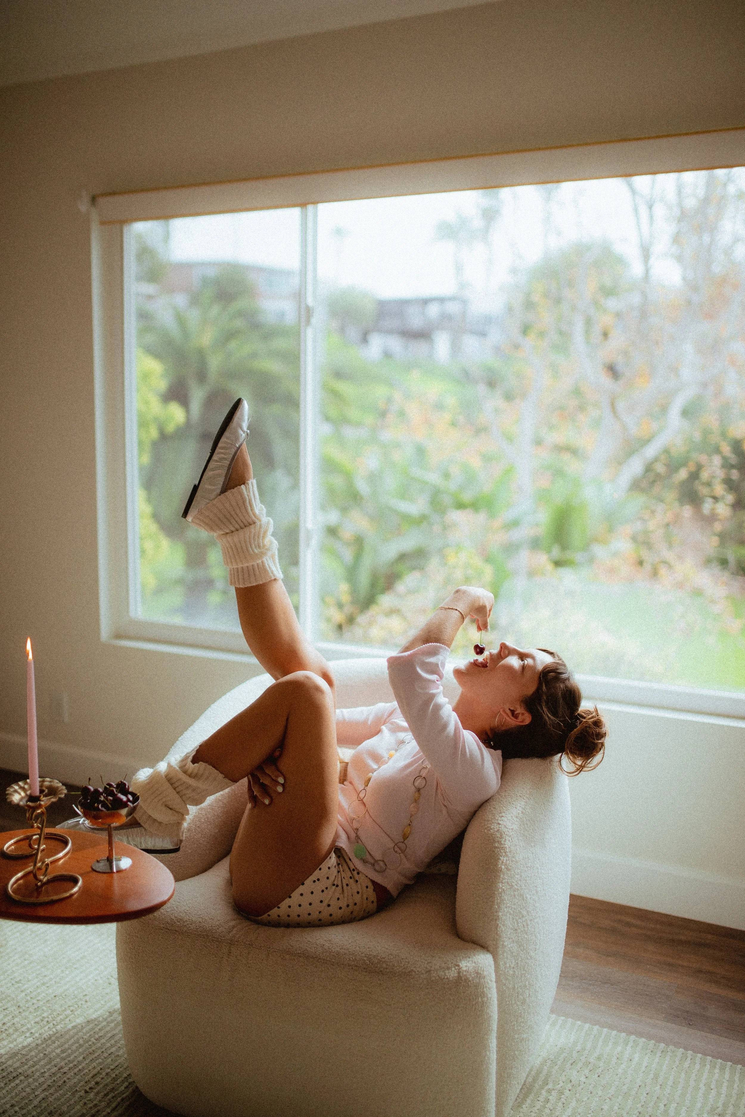 chrome glass full of dark cherries sitting on a red striped couch, Aestehtic cherry lifestyle photoshoot, Chloe Monotoya in her home in San Clemente, Cute girly aesthetic, pink candlesticks, white bubble chair, leg warmers, micro shorts and ballet fl