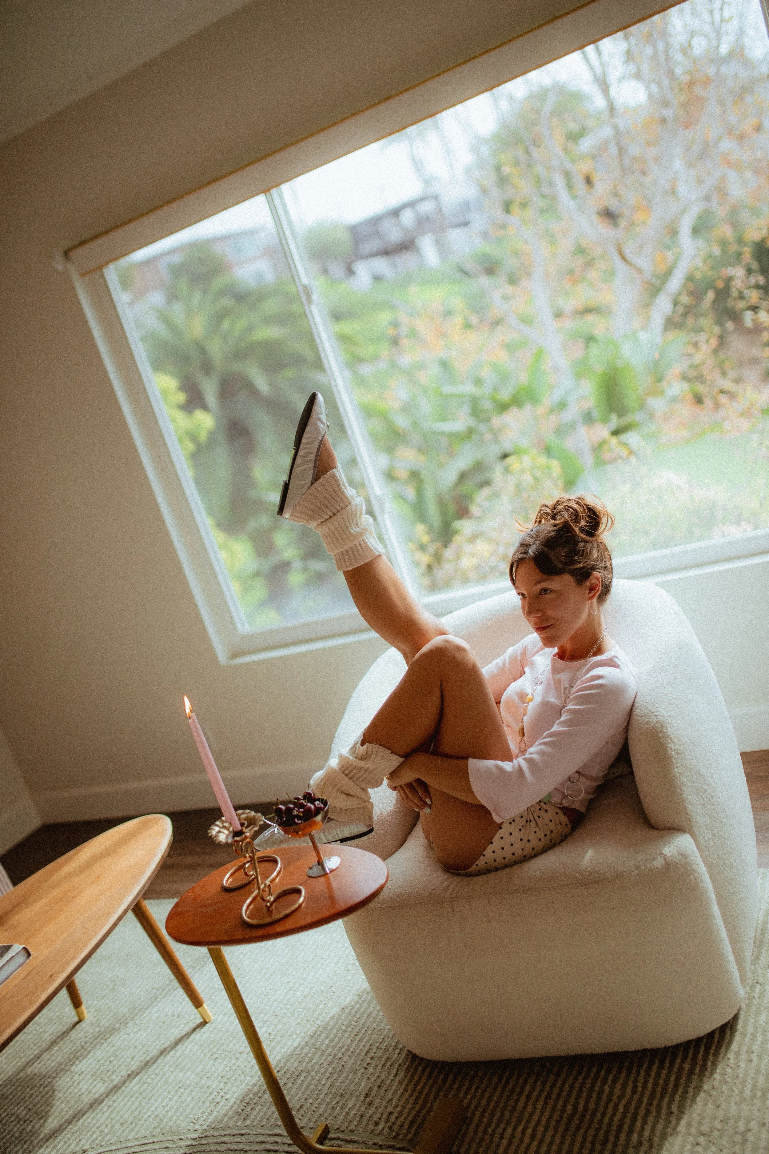 chrome glass full of dark cherries sitting on a red striped couch, Aestehtic cherry lifestyle photoshoot, Chloe Monotoya in her home in San Clemente, Cute girly aesthetic, pink candlesticks, white bubble chair, leg warmers, micro shorts and ballet fl