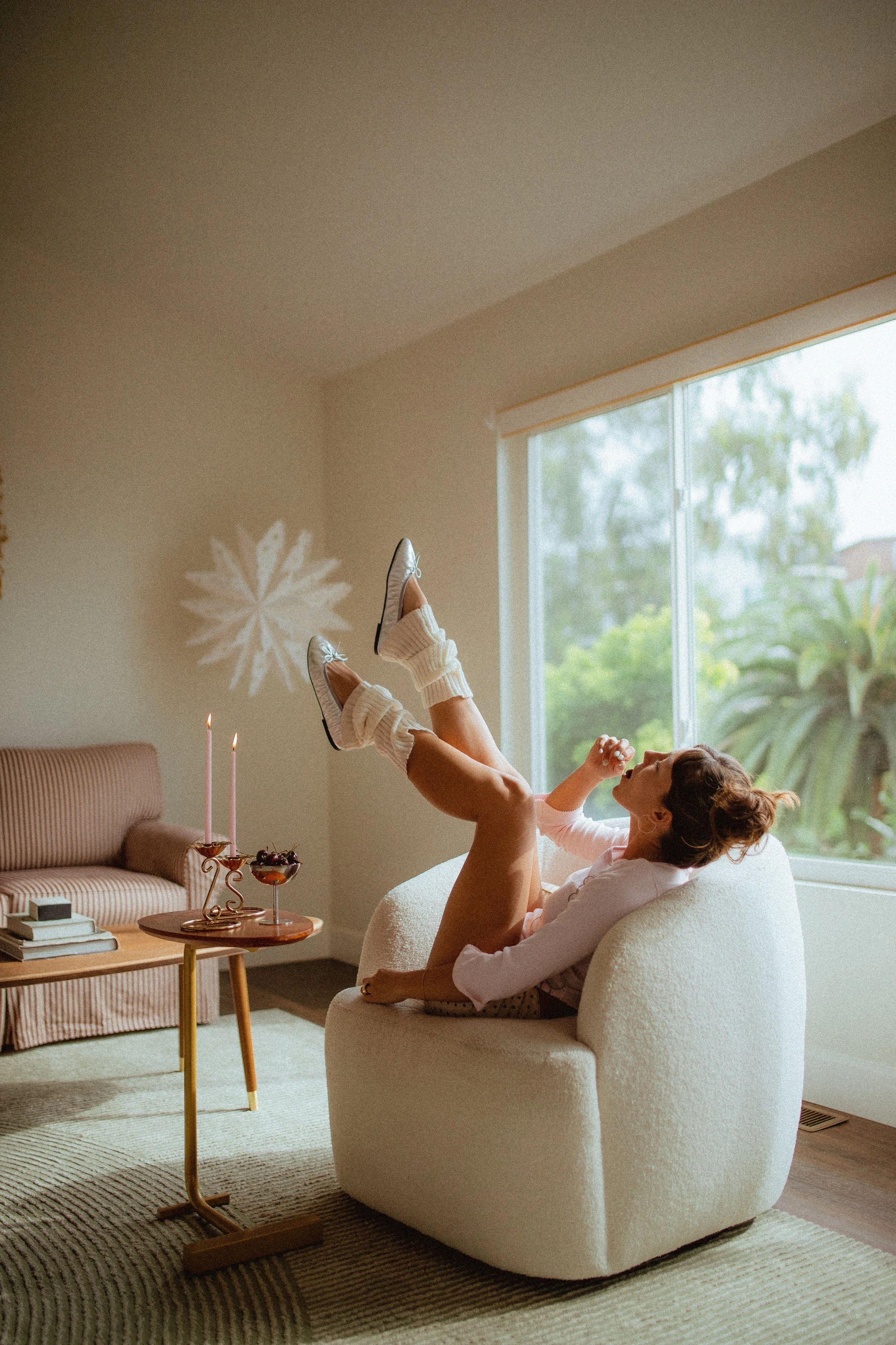 chrome glass full of dark cherries sitting on a red striped couch, Aestehtic cherry lifestyle photoshoot, Chloe Monotoya in her home in San Clemente, Cute girly aesthetic, pink candlesticks, white bubble chair, leg warmers, micro shorts and ballet fl