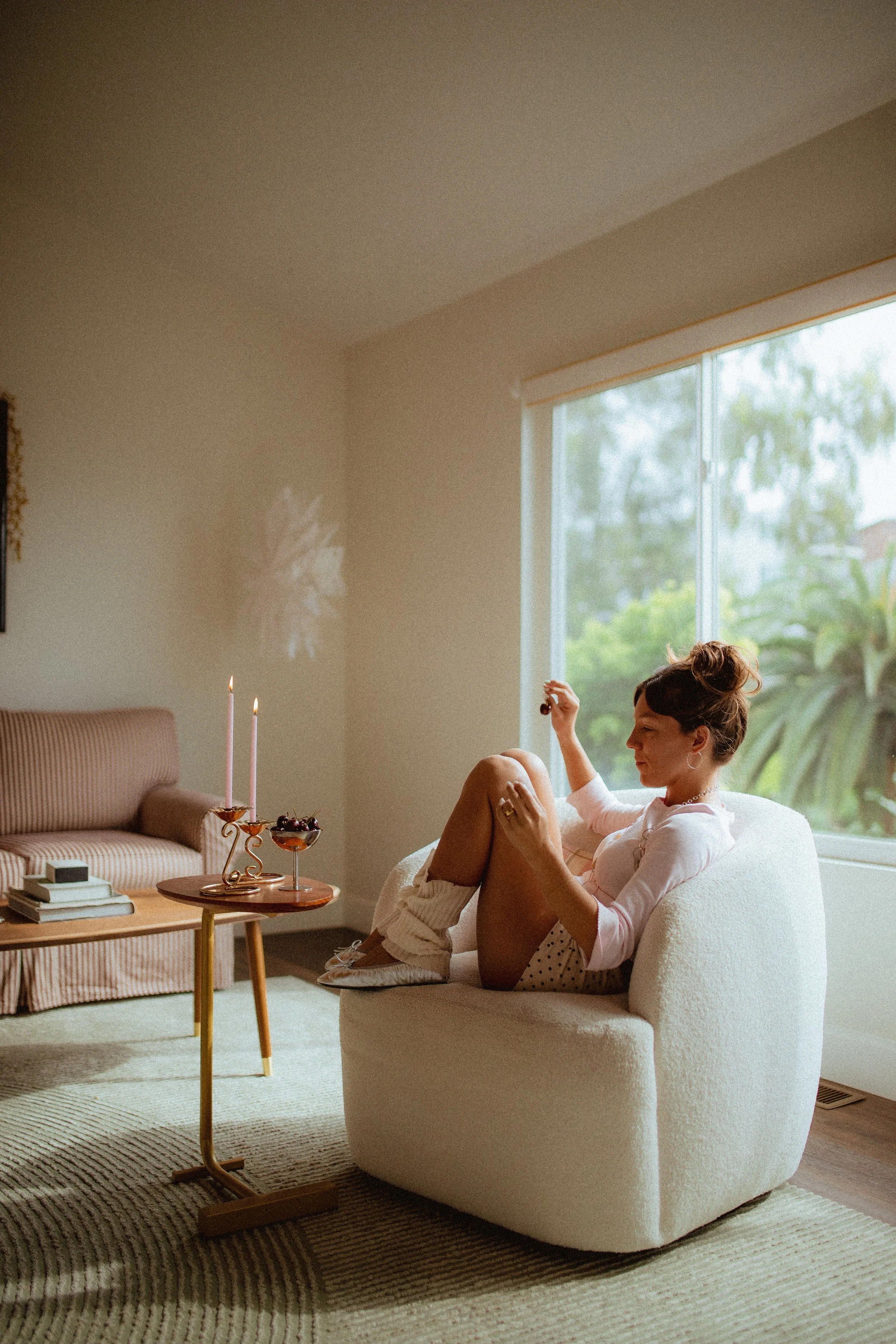 chrome glass full of dark cherries sitting on a red striped couch, Aestehtic cherry lifestyle photoshoot, Chloe Monotoya in her home in San Clemente, Cute girly aesthetic, pink candlesticks, white bubble chair, leg warmers, micro shorts and ballet fl