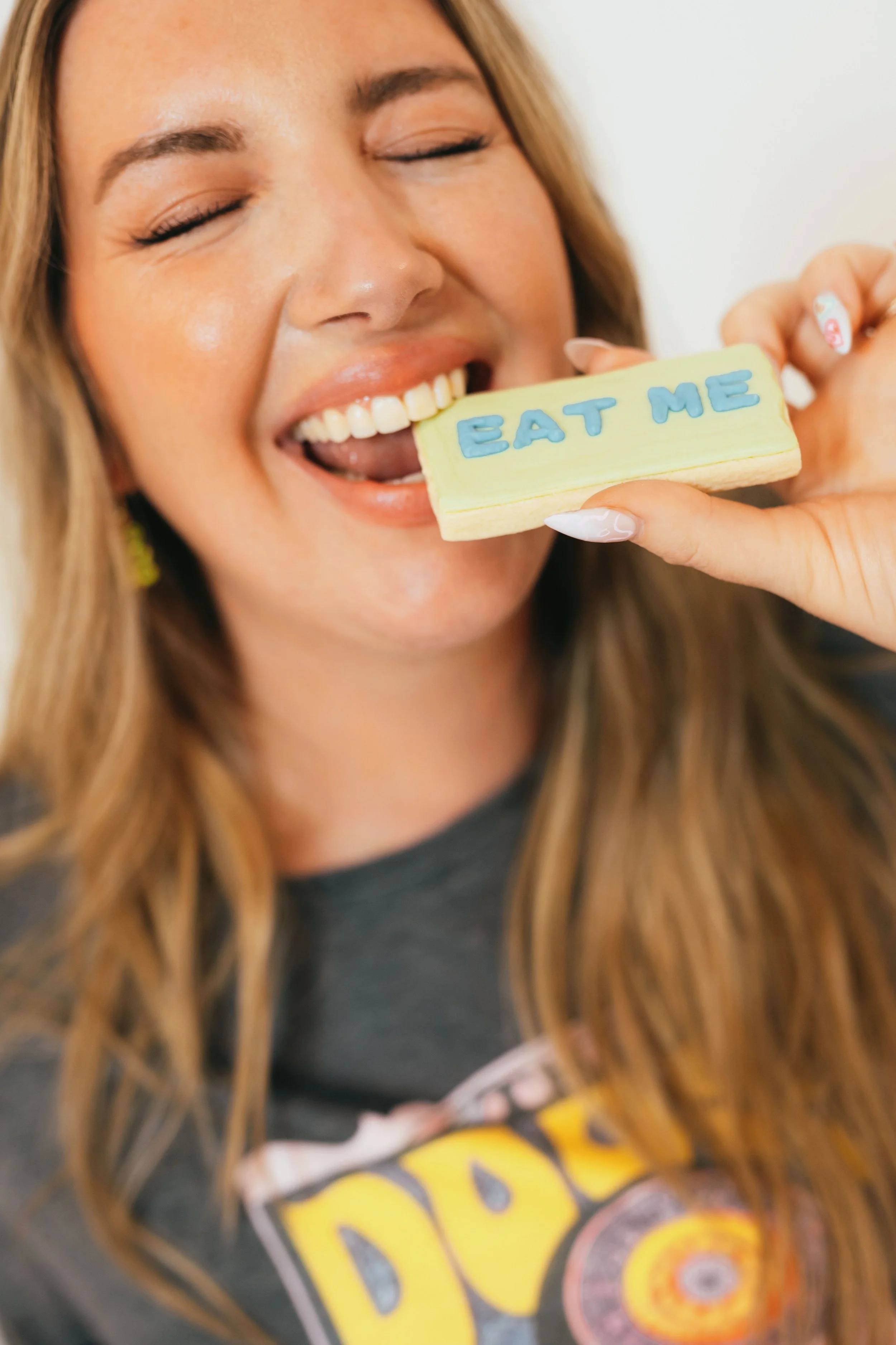 Southern California cookie decorator and home baker holding custom sugar cookie with playful expression during a colorful branding portrait photoshoot. Lifestyle marketing photography highlighting creative small business owner personality, captured b