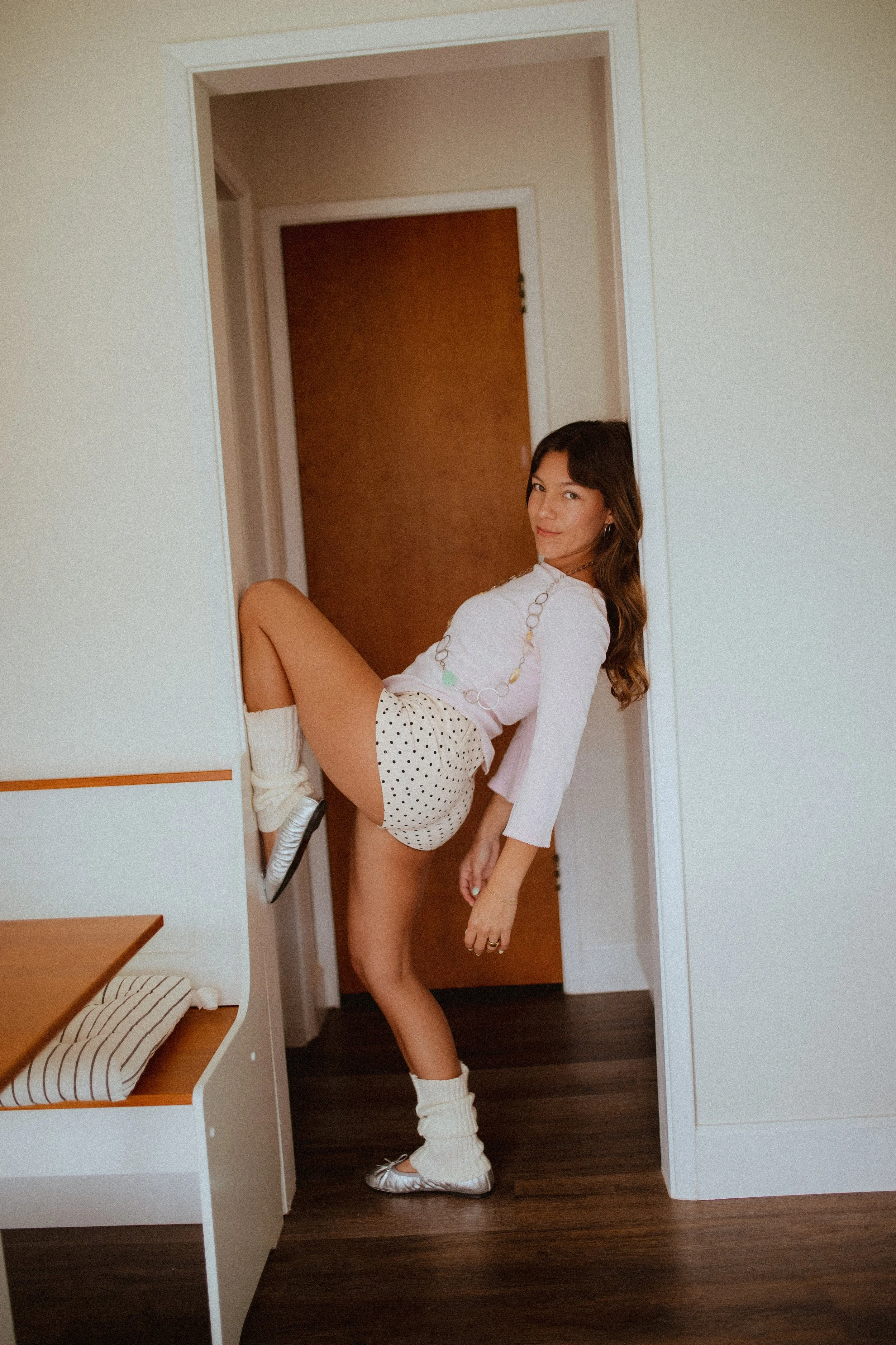 Chloe Montoya standing in her doorway in her home in orange county, CA. Creative lifestyle portrait photoshoot- standing ina. fun and unique way in home photoshoot, Wearing, Ballet flats, leg warmers and micro shorts. POsing inspiration for creative 