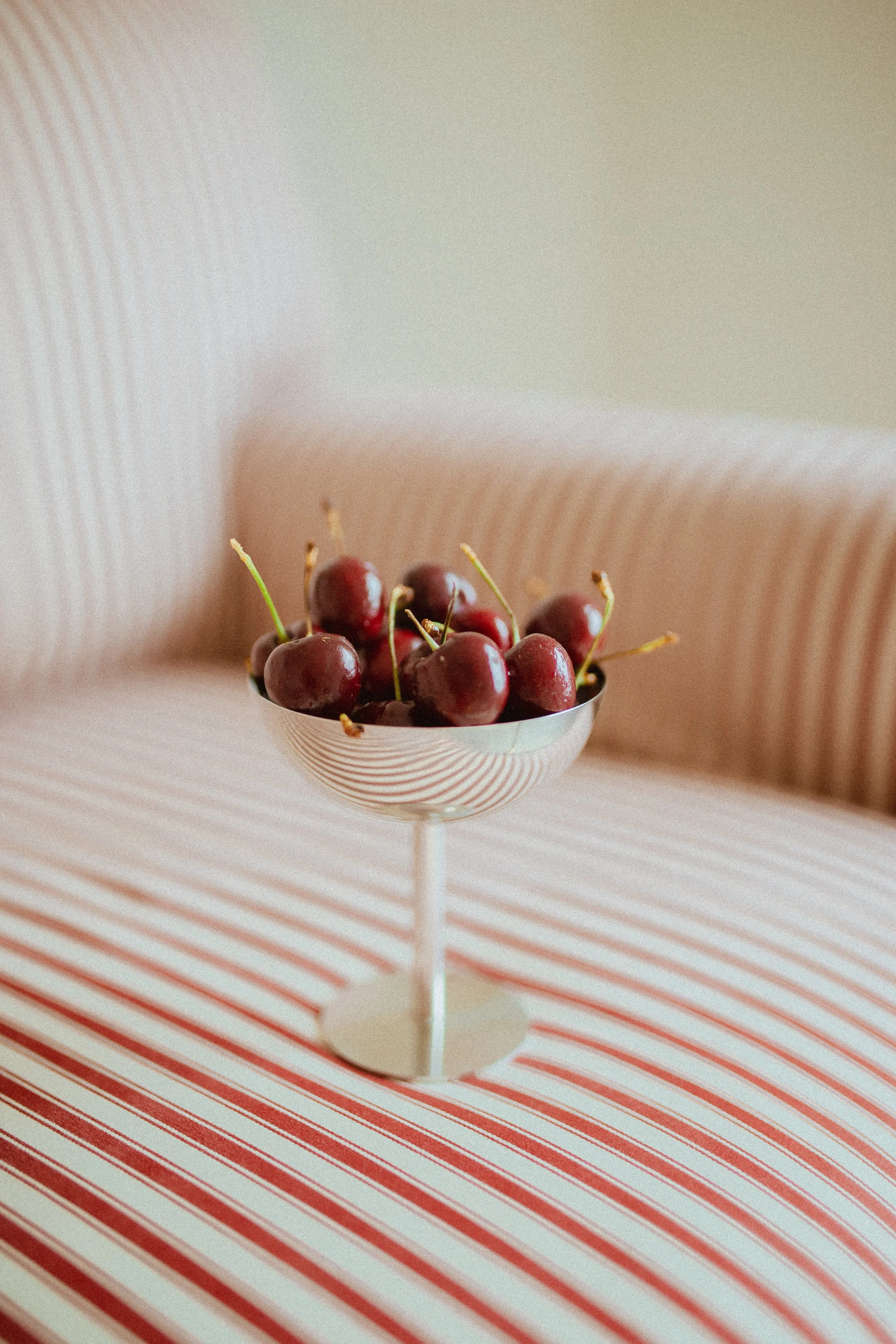 chrome glass full of dark cherries sitting on a red striped couch, Aestehtic cherry lifestyle photoshoot