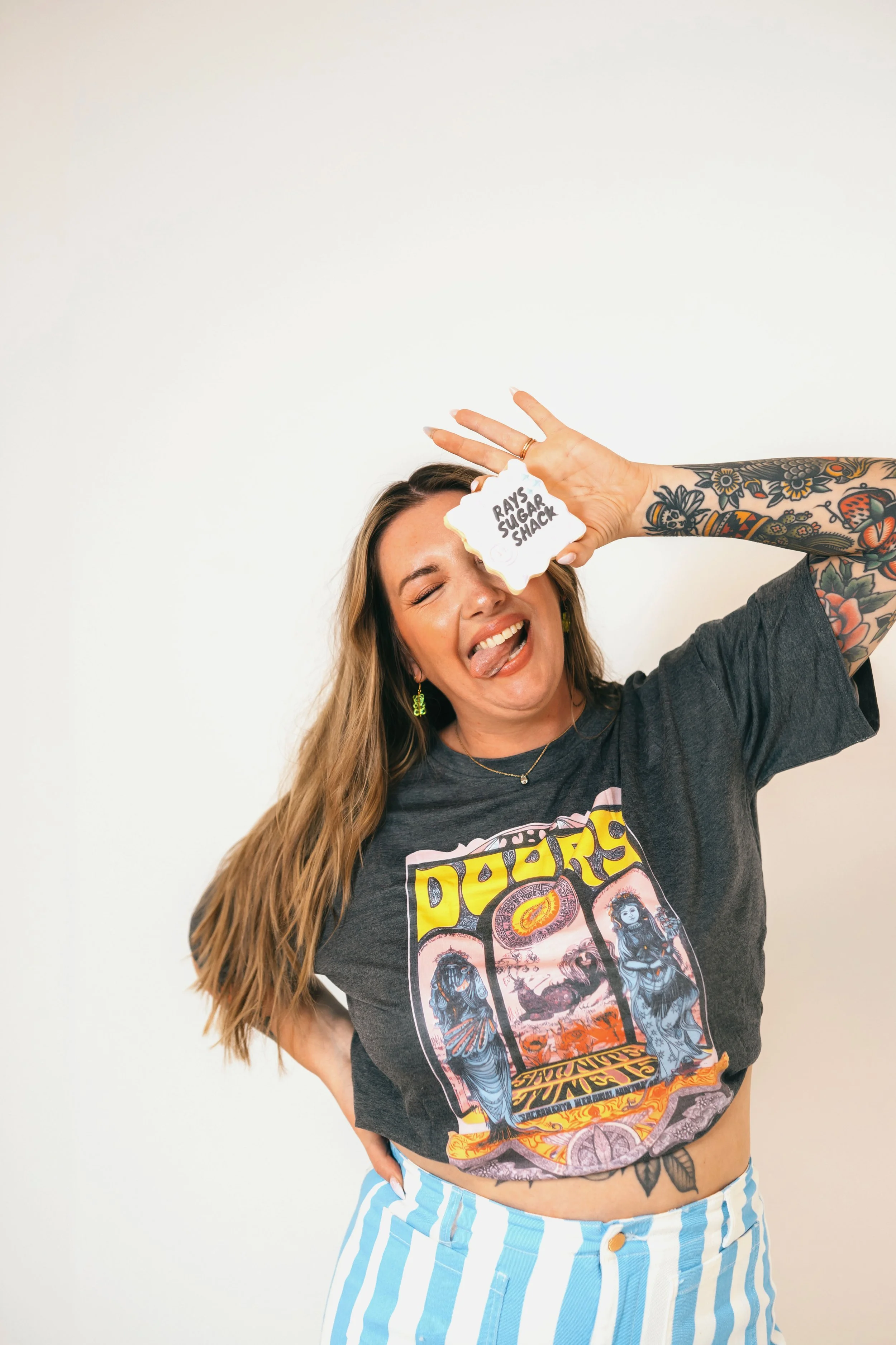 Southern California cookie decorator and home baker holding custom sugar cookie with playful expression during a colorful branding portrait photoshoot. Lifestyle marketing photography highlighting creative small business owner personality, captured b