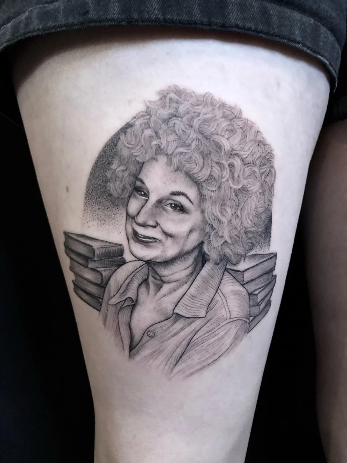 Fine line and black and grey celebrity tattoo portrait of Margaret Atwood with stacks of books behind her, created by Seattle tattoo artist Eli Bischof.
