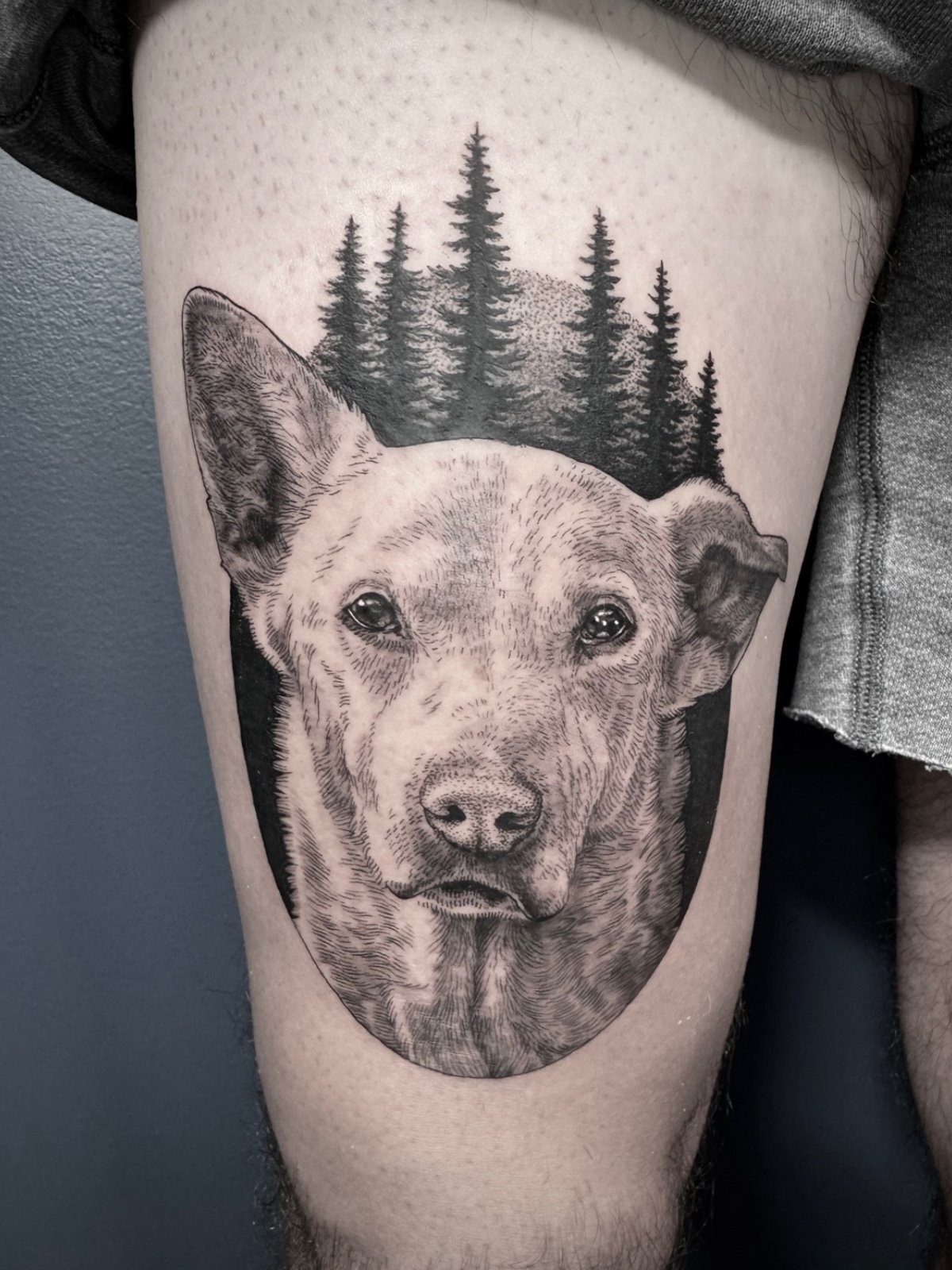 Fine line and black and grey pet portrait tattoo of a white dog in a PNW forest setting, created by Seattle tattoo artist Eli Bischof.