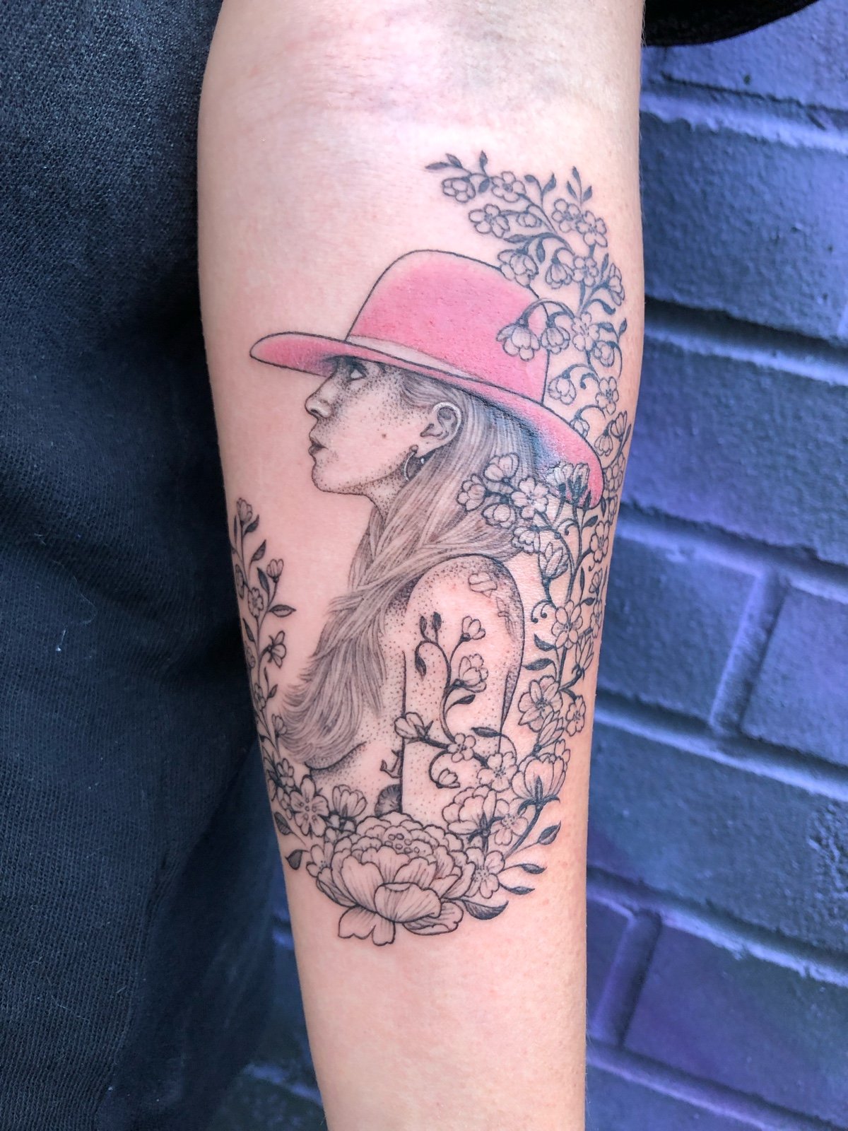 Fine line and black and grey celebrity tattoo portrait of Lady Gaga wearing a pink cowboy hat, with delicate flowers, vines, and leaves, created by Seattle tattoo artist Eli Bischof.
