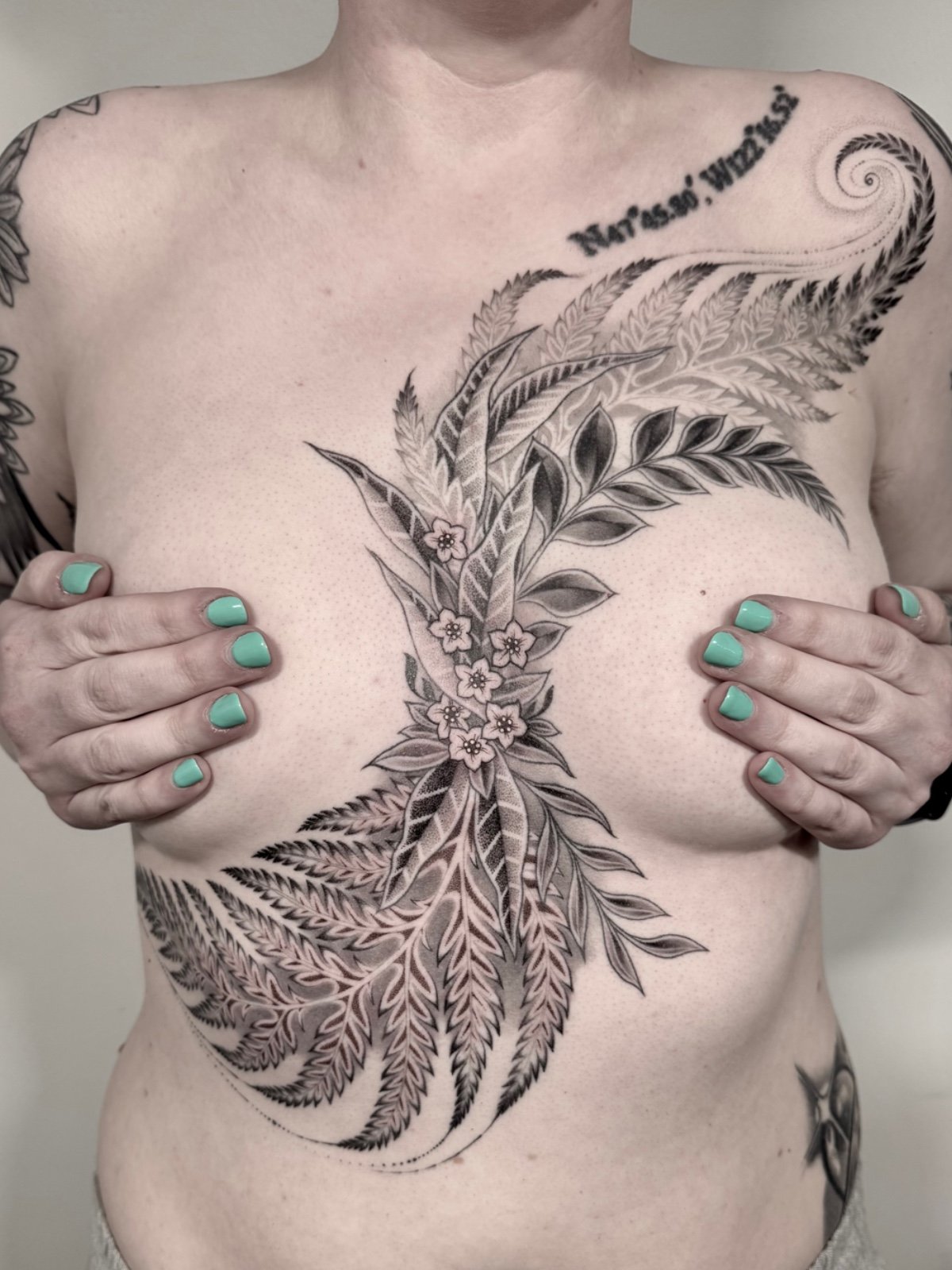 A large fine line and black and grey botanical tattoo flowing across chest and torso, with ferns, leaves, and flowers, created by Eli Bischof in Seattle.