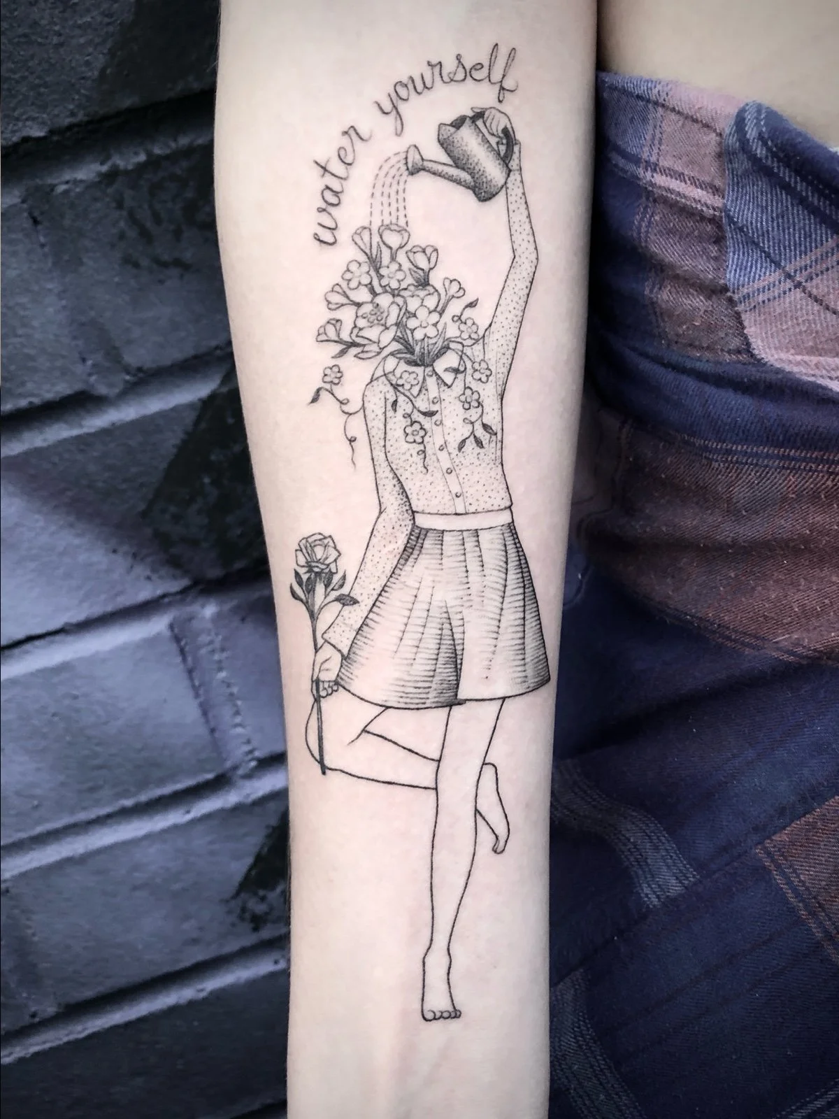 A fine line and black and grey tattoo of a young woman with a head made of flowers, holding a watering can over her head and watering herself, created by Seattle tattoo artist Eli Bischof.