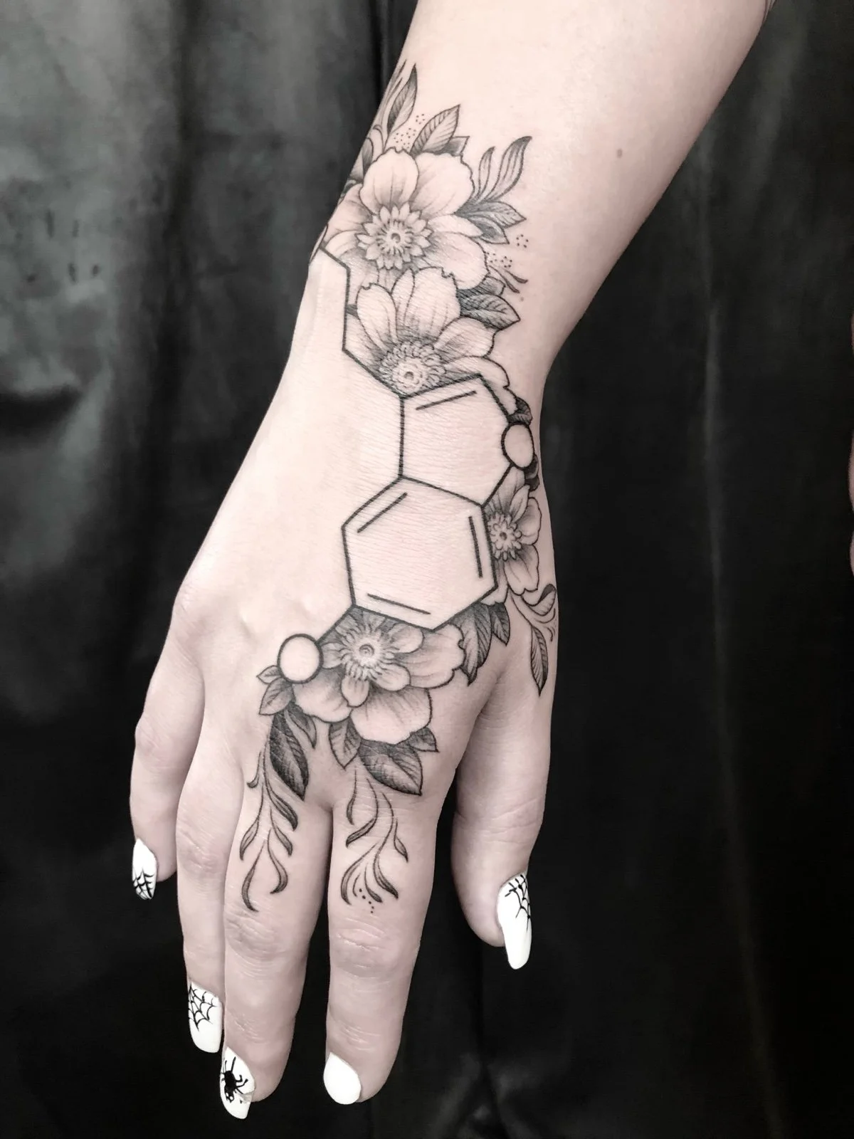 Fine line black and grey hand tattoo with flowers, leaves, and serotonin symbol, created by Seattle tattoo artist Eli Bischof